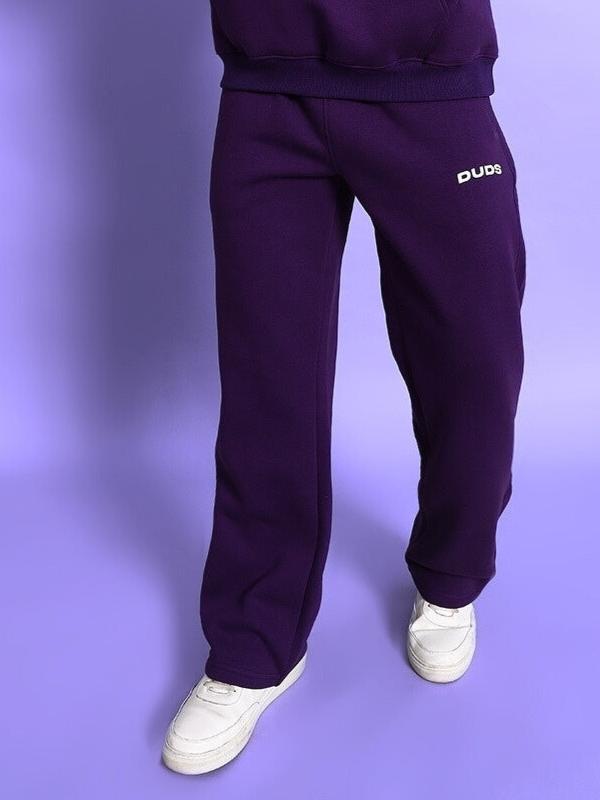 Person wearing SOOTY COTTON FLEECE PANT PURPLE, showcasing comfortable streetwear style with elastic waistband and ribbed cuffs.