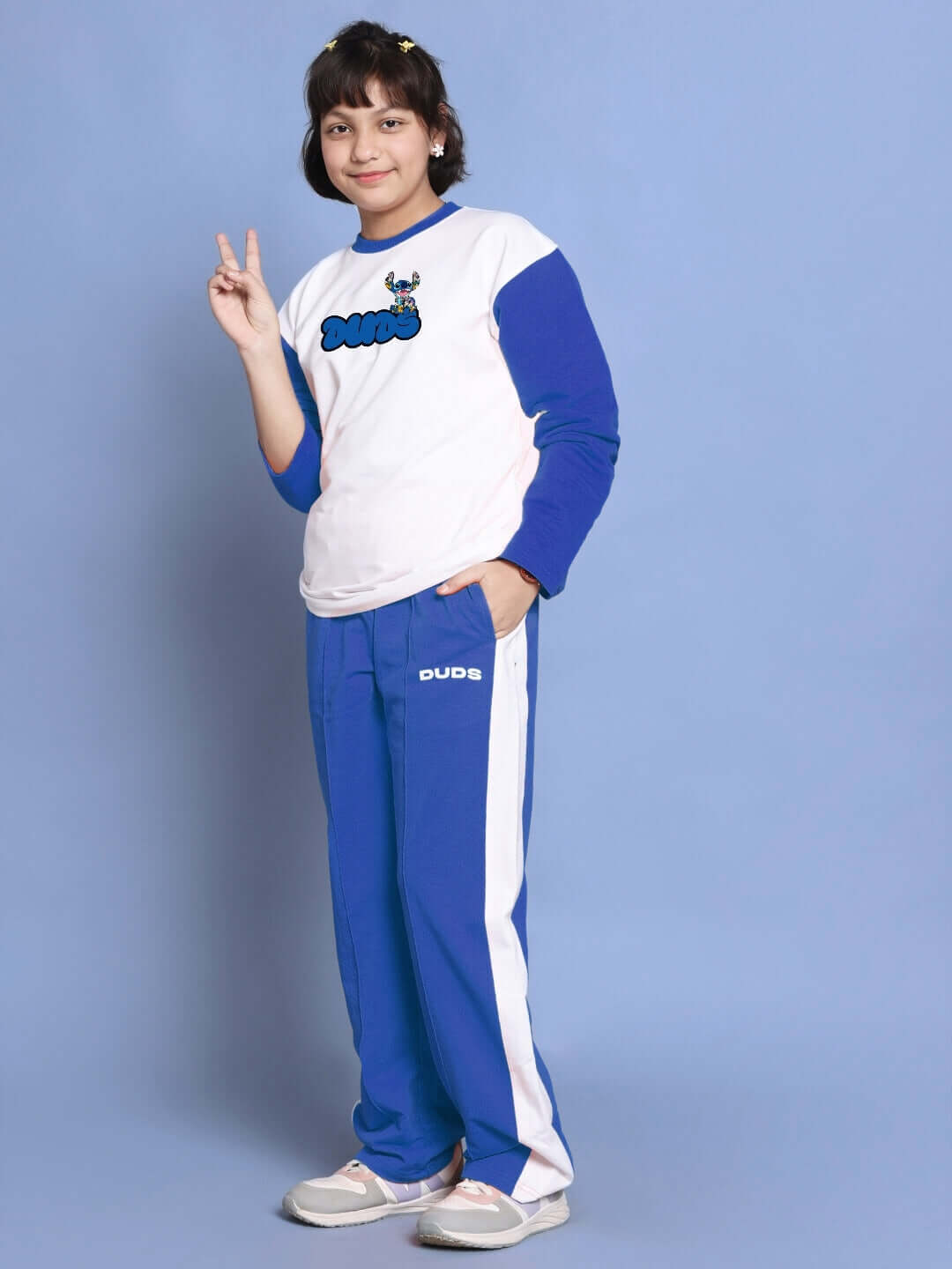 Child wearing white-blue oversized co-ord set with relaxed fit joggers and drawstring waistband, posing against a blue background.