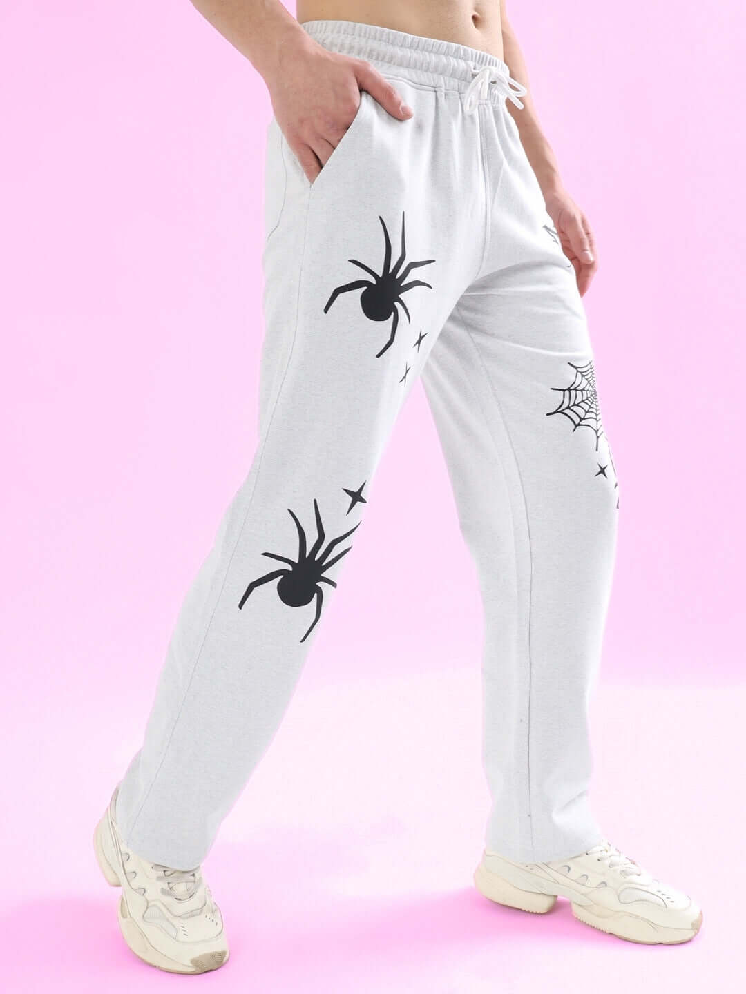 Model wearing light grey relaxed joggers with spider web design, showcasing comfortable fit against a pink background.