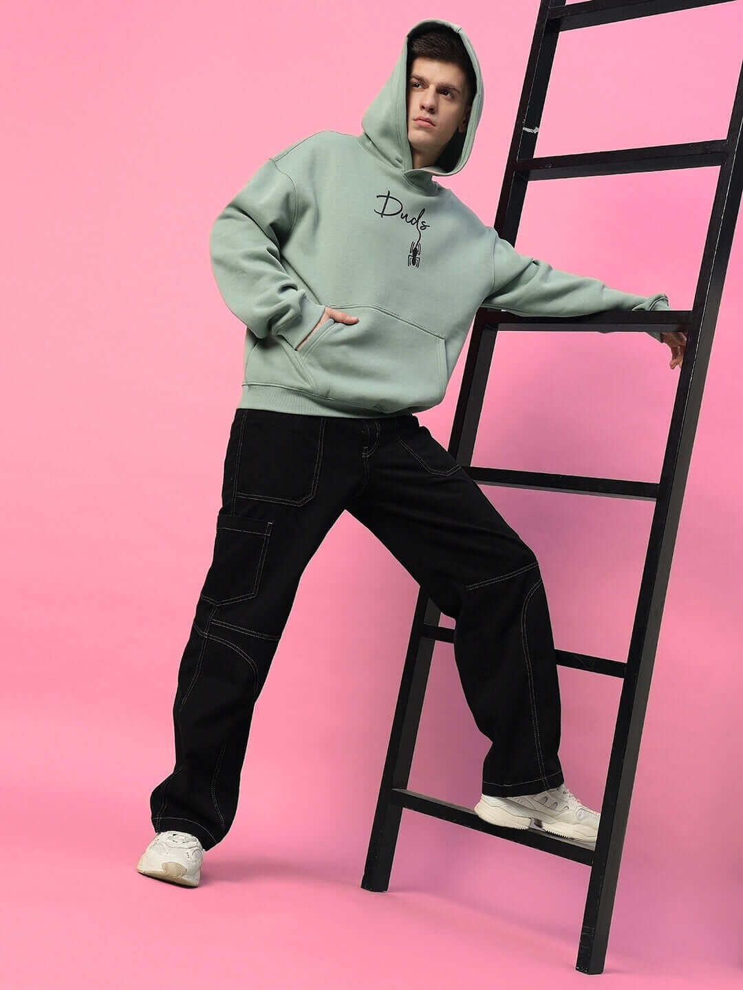 Model wearing SPIDERMAN OVERSIZED FLEECE HOODIE JADE GREEN against pink background, showcasing relaxed streetwear style.