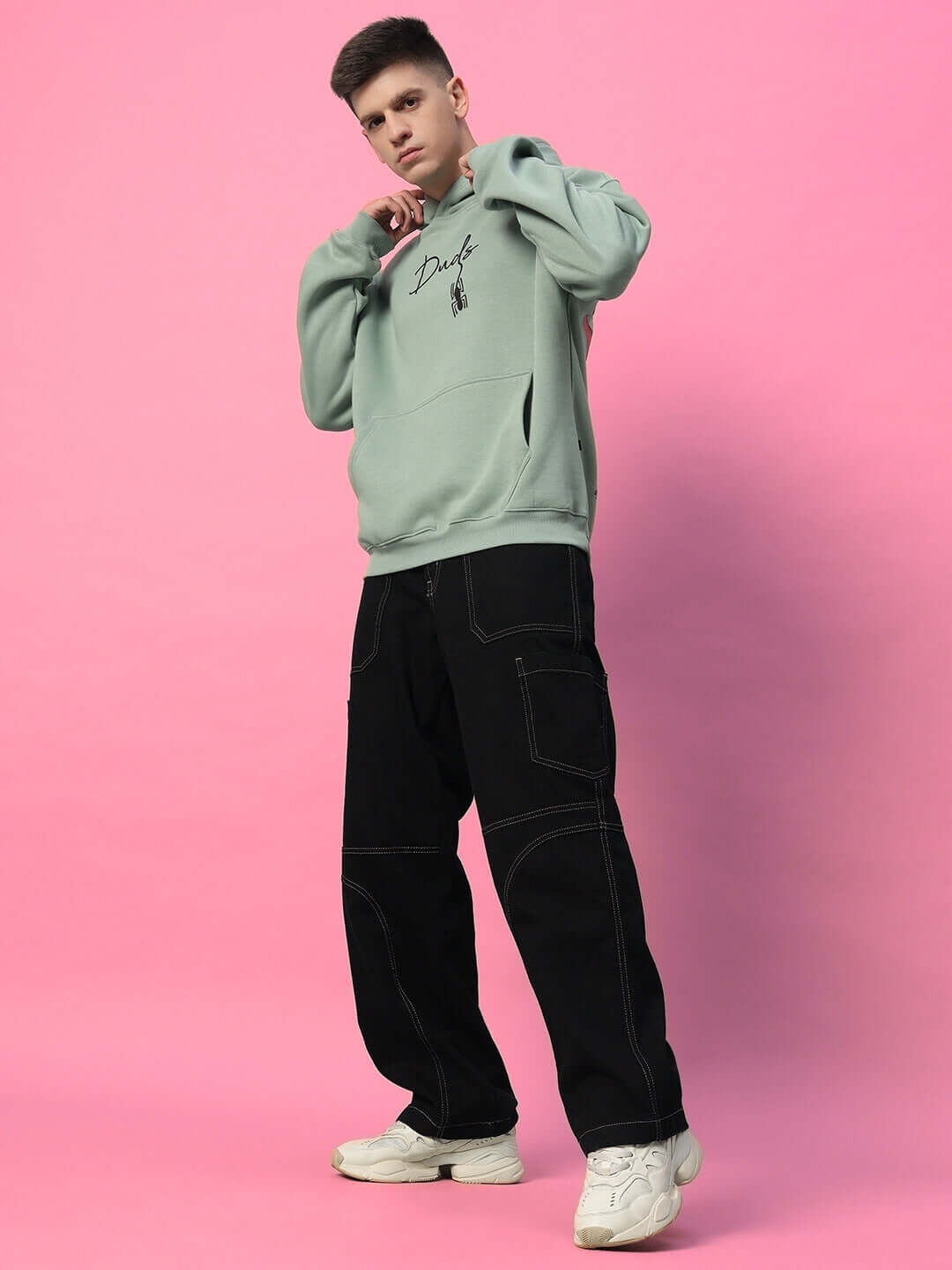 Model wearing SPIDERMAN OVERSIZED FLEECE HOODIE JADE GREEN, paired with black pants, showcasing trendy streetwear style.