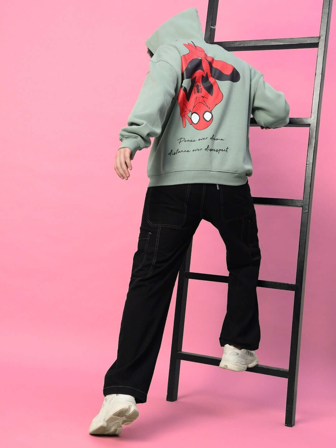 Person wearing SPIDERMAN OVERSIZED FLEECE HOODIE JADE GREEN, climbing a ladder, showcasing Spiderman graphic on back.