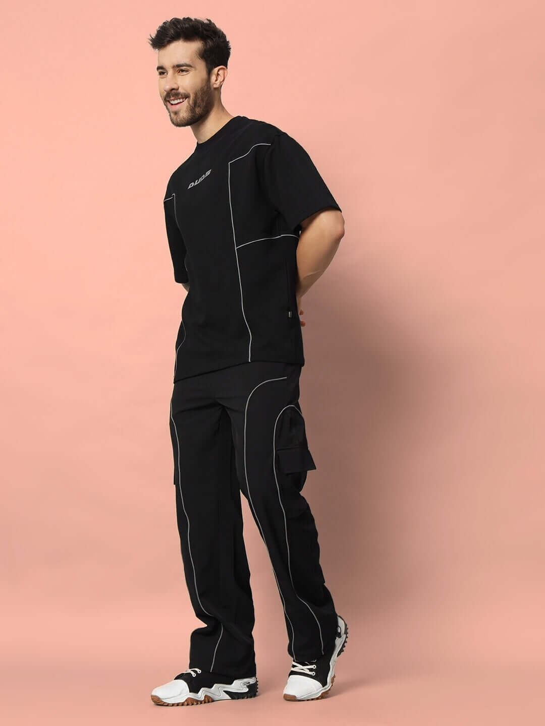 Model wearing black oversized t-shirt made of premium cotton and elastane, showcasing casual style against a peach background.