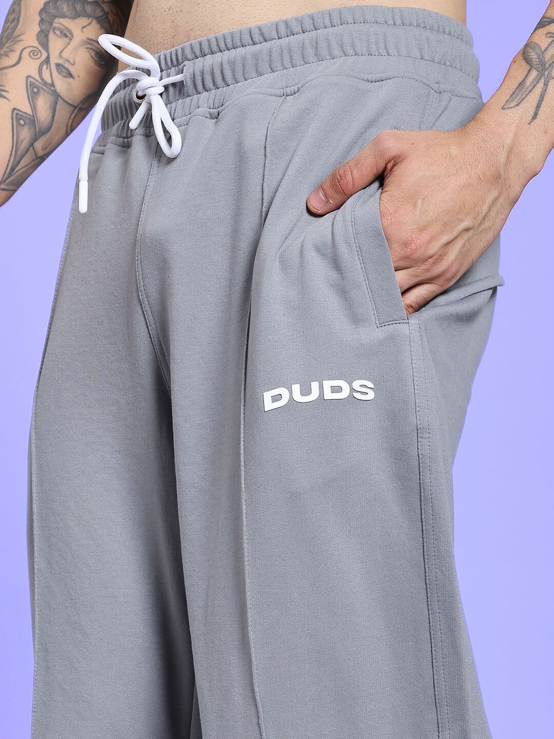 Person wearing SPIRAL RELAXED-FIT JOGGERS GREY with a hand in the pocket against a purple background.