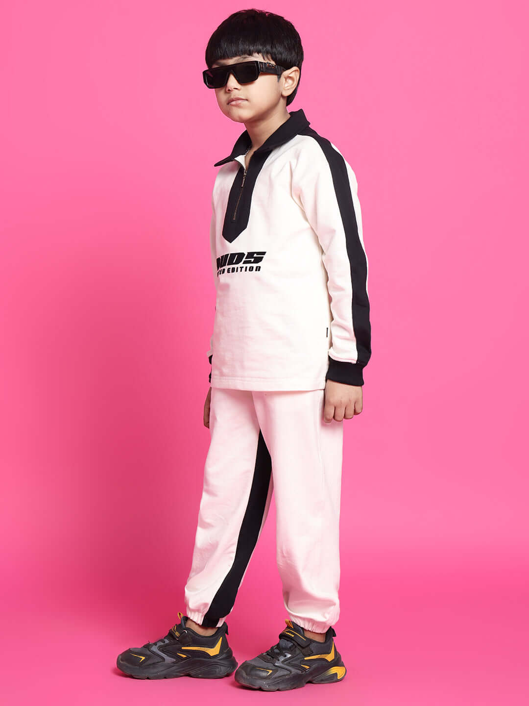 Child wearing SPLINTER OVERSIZED CO-ORD SET FOR BOYS GIRLS OFF WHITE BLACK with stylish sunglasses against a pink background.