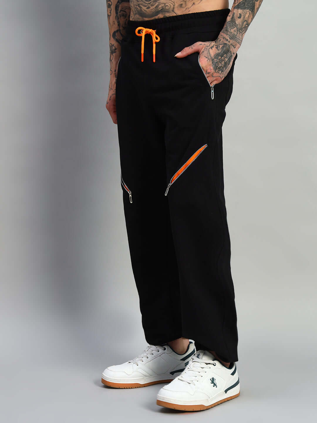 Black SQUALL joggers with orange drawstring and zippers, worn with white sneakers, designed by DUDS.