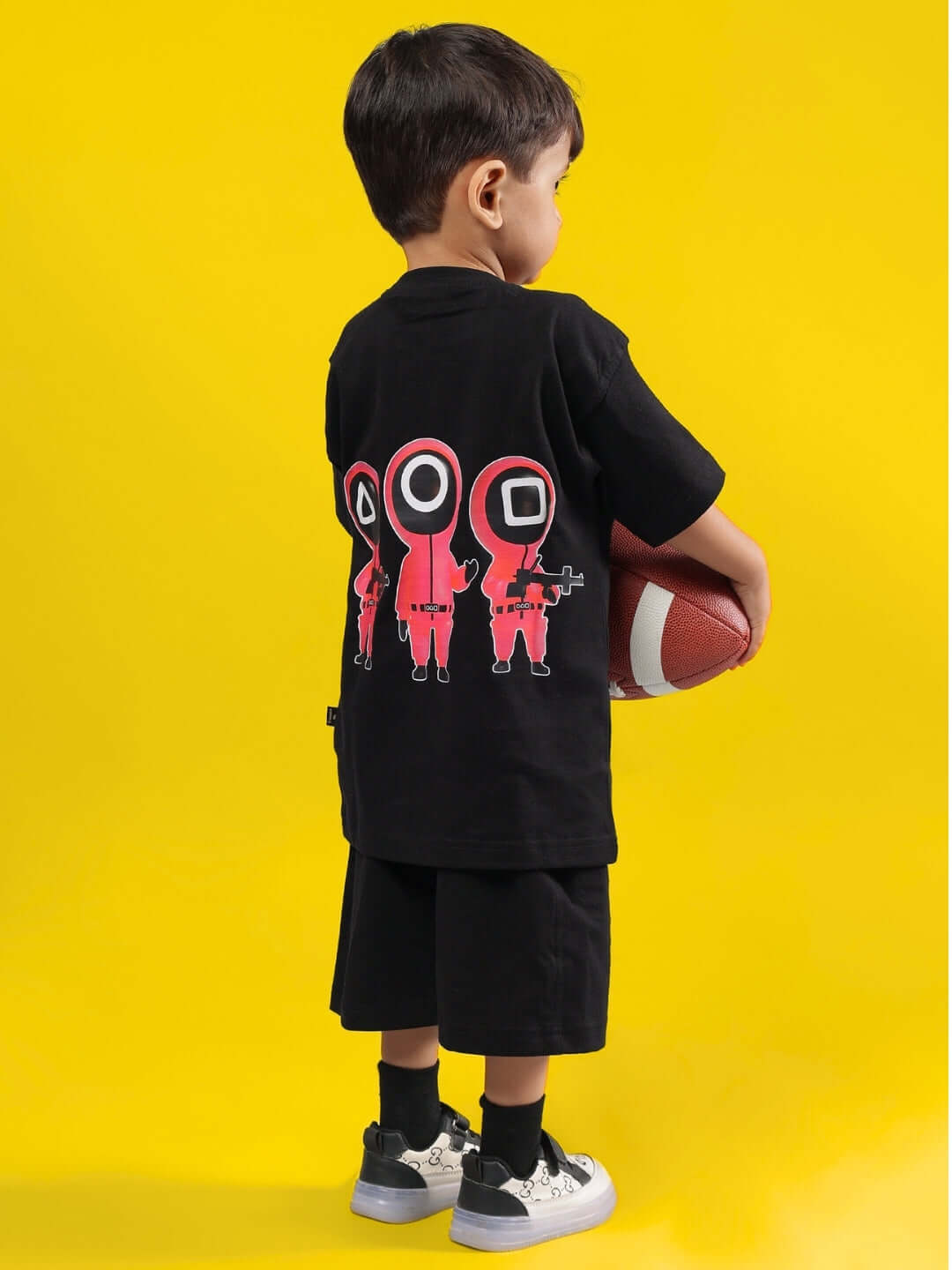 Child wearing black Squid Battle Co-ord set, holding a football, featuring vibrant red graphics on the back.