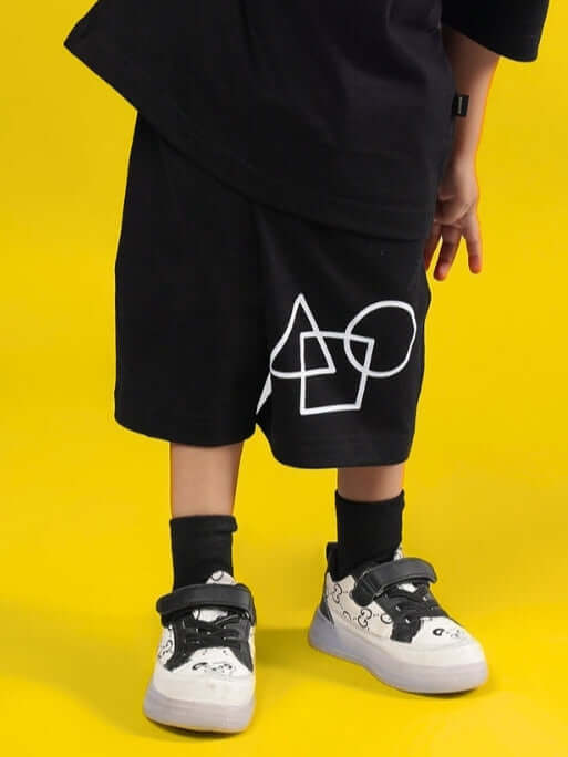 Child wearing black Squid Battle Shorts with geometric design by DUDS on yellow background.