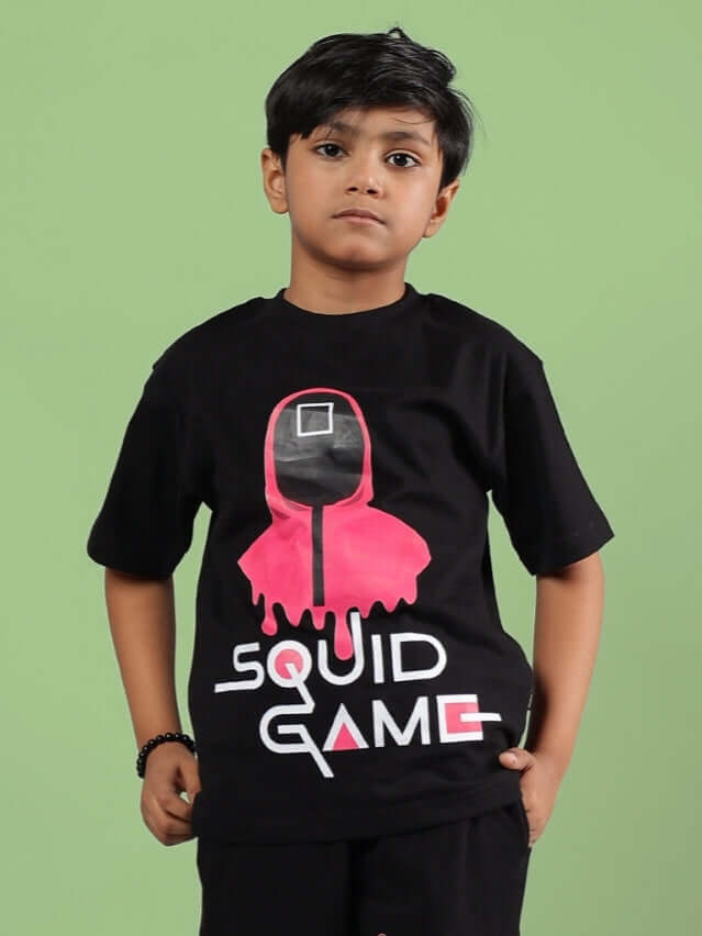 Young boy wearing a black Squid Game t-shirt with a graphic design, standing against a green background.