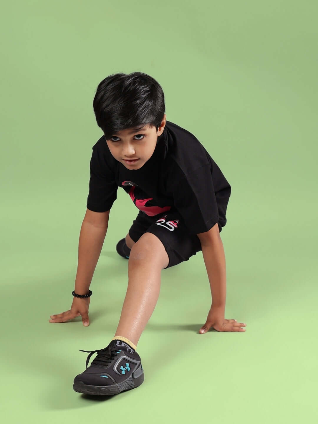 Boy wearing black Squid Games co-ord set from DUDS on a green background, showcasing a dynamic pose.