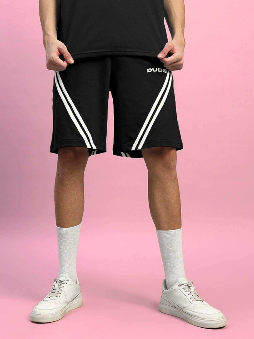 Person wearing STAR JUMPER Regular Fit Black Shorts with white stripes, customizable size option, standing on a pink background.