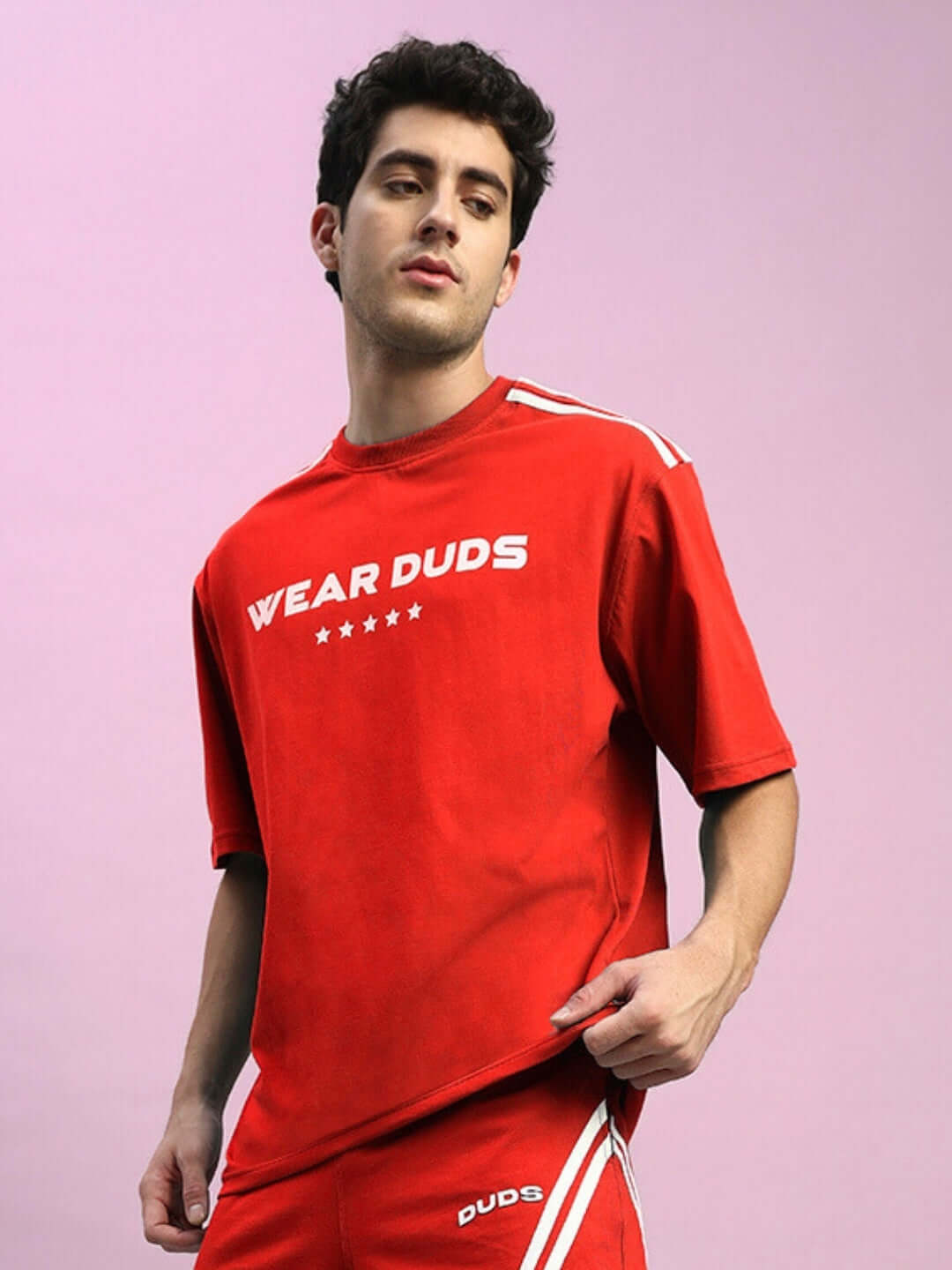 Model wearing red STAR JUMPER over-sized t-shirt made of premium cotton, featuring bold design, on a pastel background.