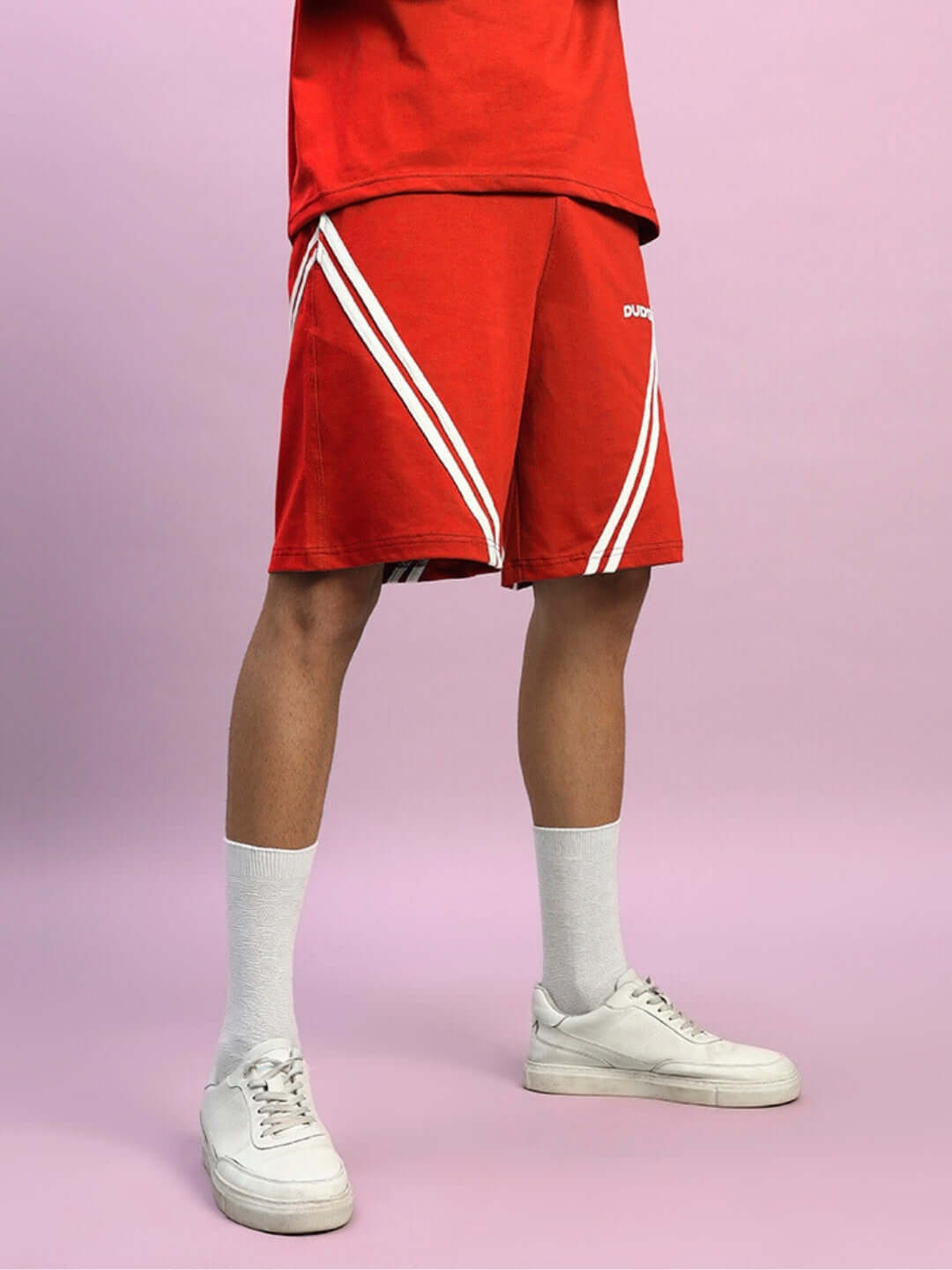 Red STAR JUMPER Regular Fit Shorts with white stripes, customizable size available, shown with white sneakers and socks, on pink backdrop.