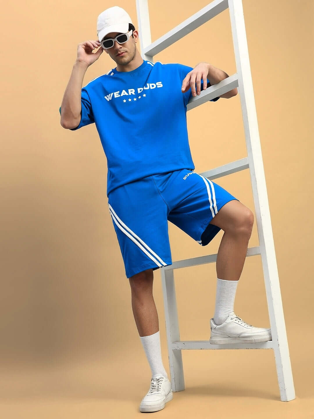 Model wearing STAR JUMPER Regular Fit Shorts in Royal Blue, styled with a matching blue top, white sneakers, and sunglasses.