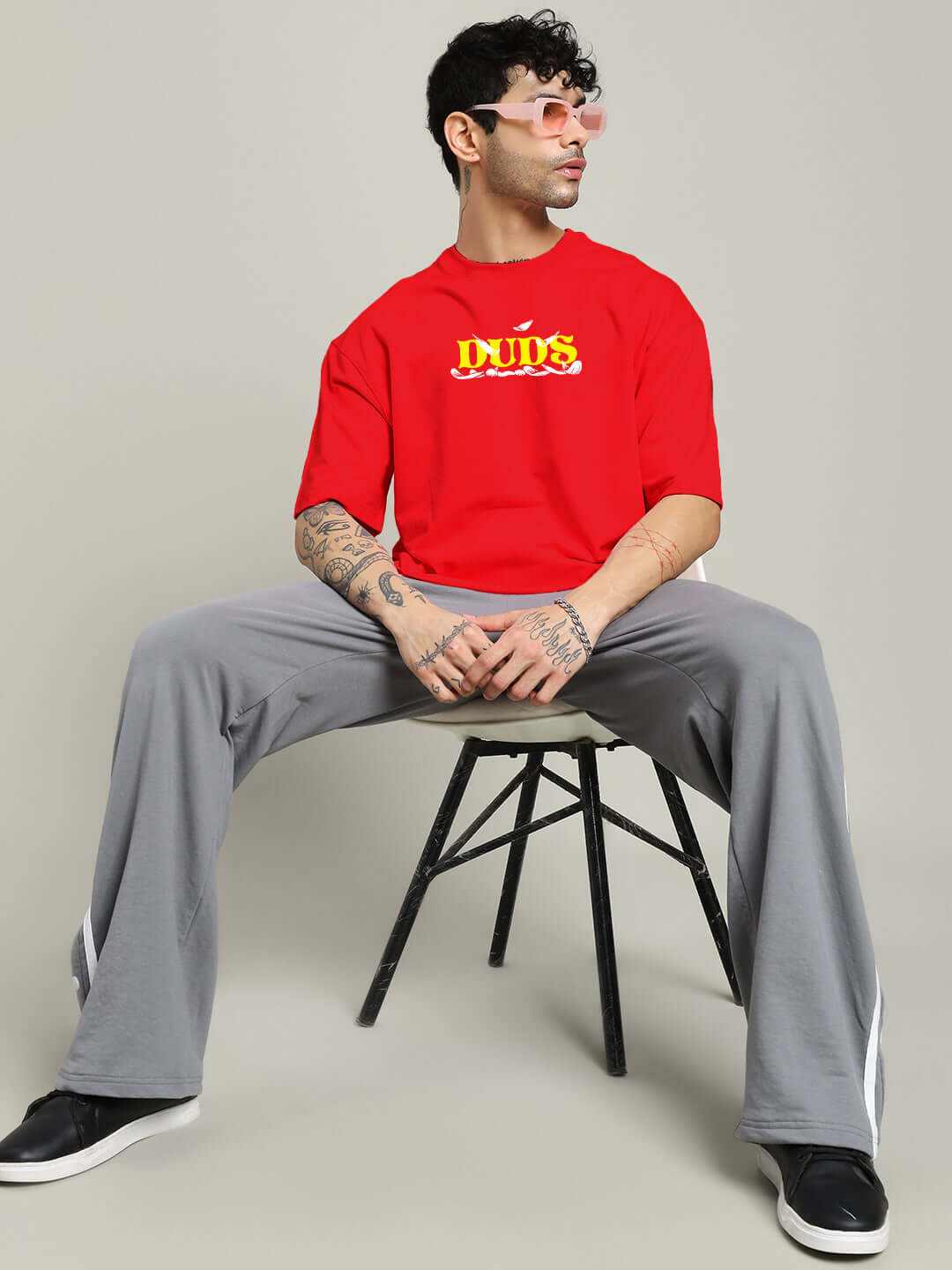 Alt Tag: Man wearing STAY HAPPY PRINTED OVERSIZED T-SHIRT RED sitting stylishly with casual gray pants.