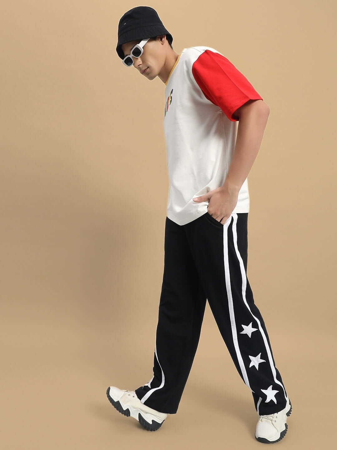 Model wearing Stellar Relaxed Joggers in black, featuring star design, showcasing casual fashion style with white sneakers and a hat.