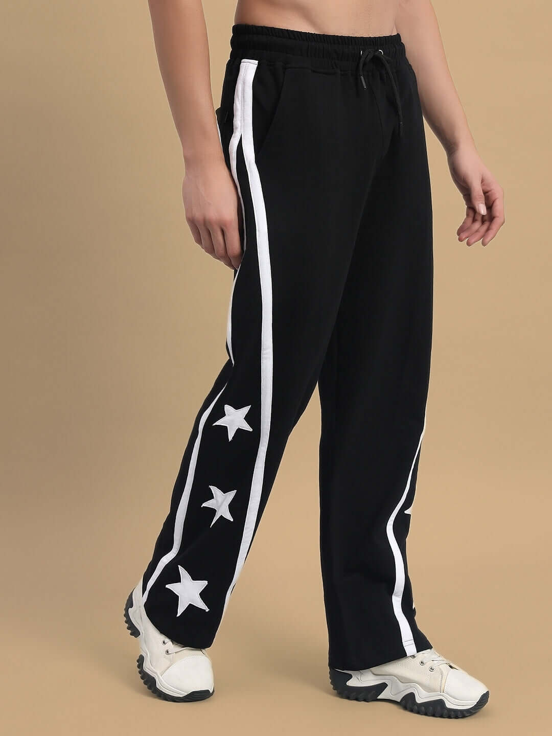 Person wearing black Stellar Relaxed Joggers with white star design and stripes, showcasing comfortable and casual fit by DUDS.