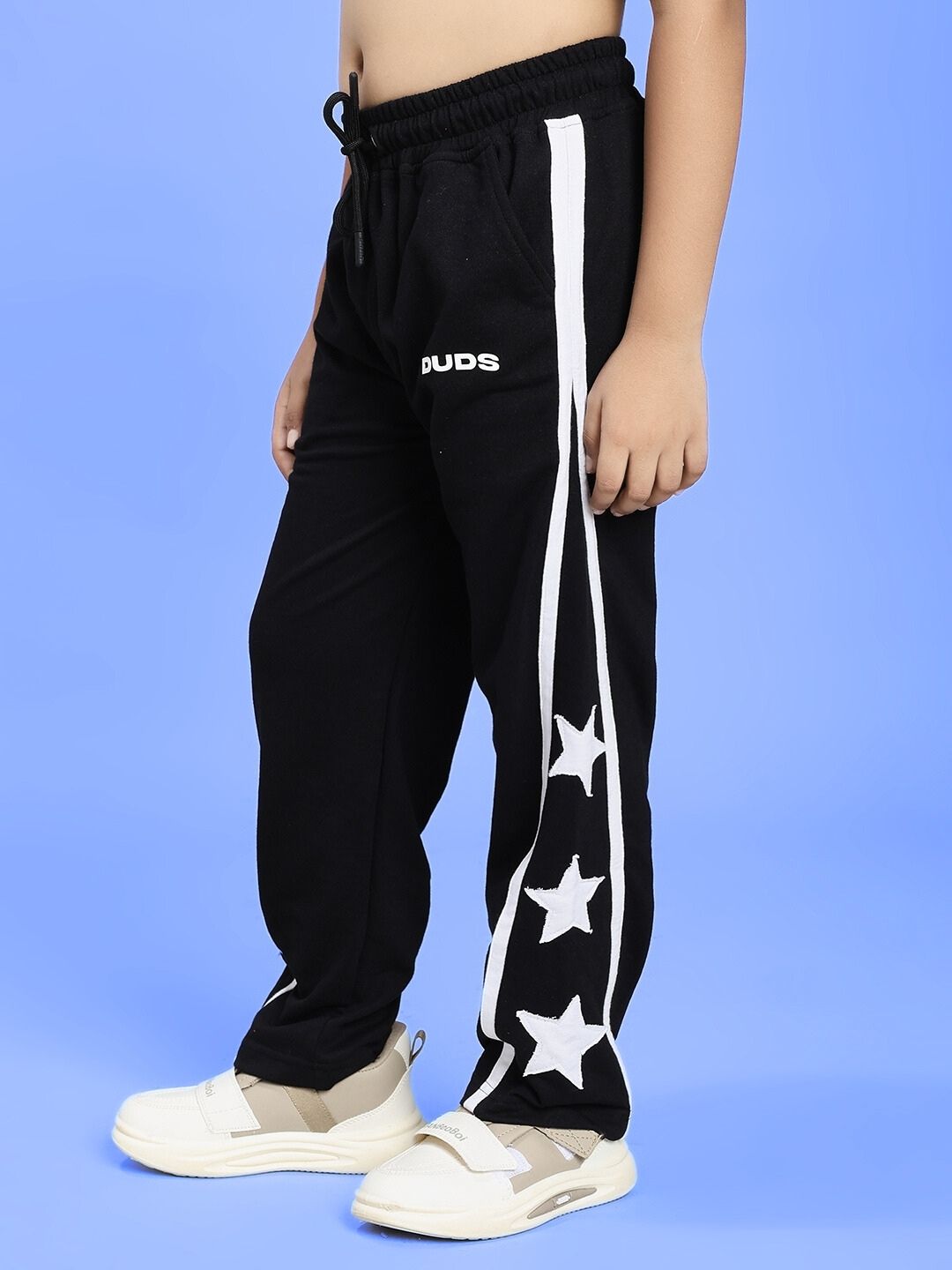 Boy wearing STELLAR RELAXEDFIT JOGGER FOR BOYS AND GIRLS BLACK with white stars design on blue background.