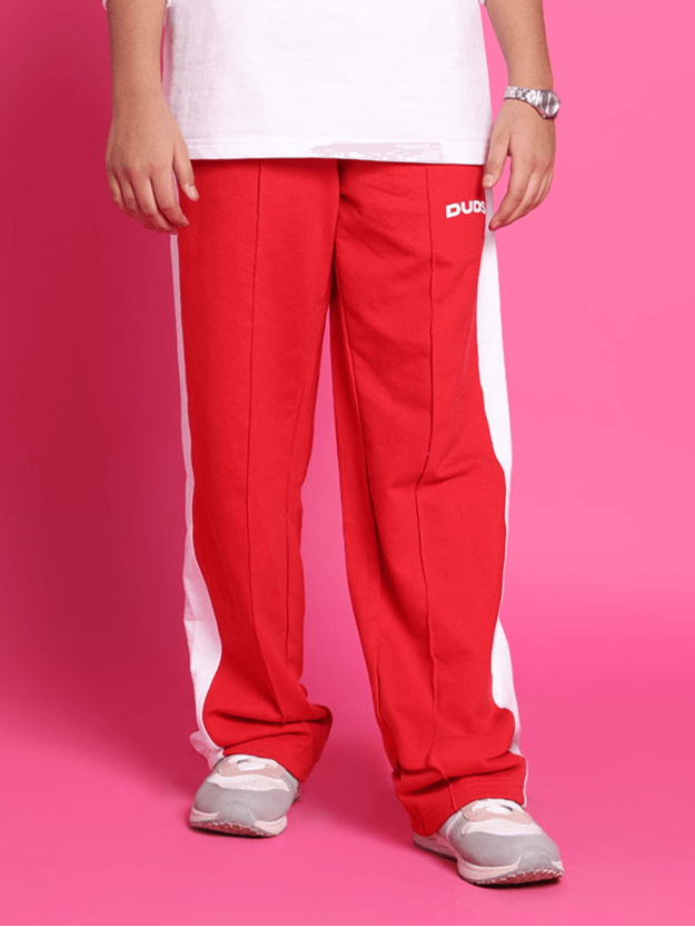 Child wearing red stitch jogger pants for boys and girls by DUDS, featuring white side stripes and a relaxed fit, against a pink background.