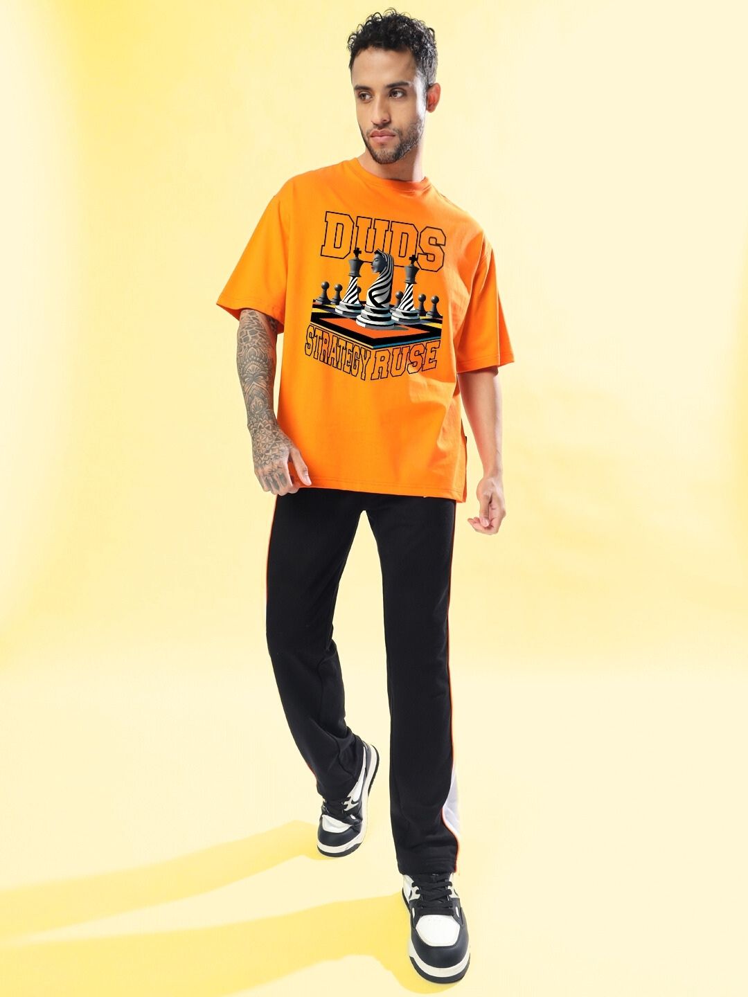 Model wearing STRATEGY RUSE OVER-SIZED T-SHIRT ORANGE with bold graphic design, showcasing streetwear style and vibrant color.