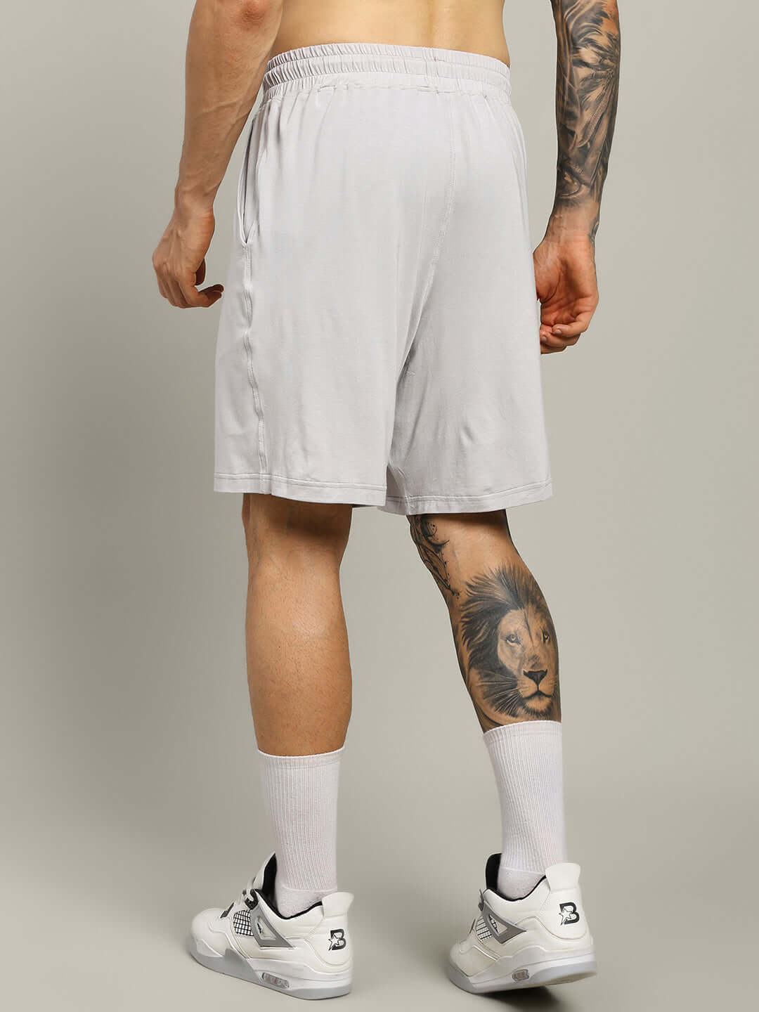 Man wearing light grey STRENGTH FREAK shorts, showcasing a comfortable fit, with tattooed leg visible, ideal for custom size options. 