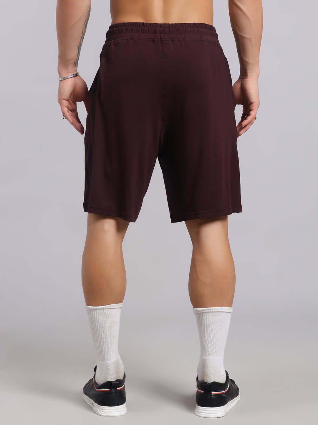 Back view of wine-colored STRENGTH FREAK SHORTS showcasing relaxed fit, worn by model with socks and sneakers.