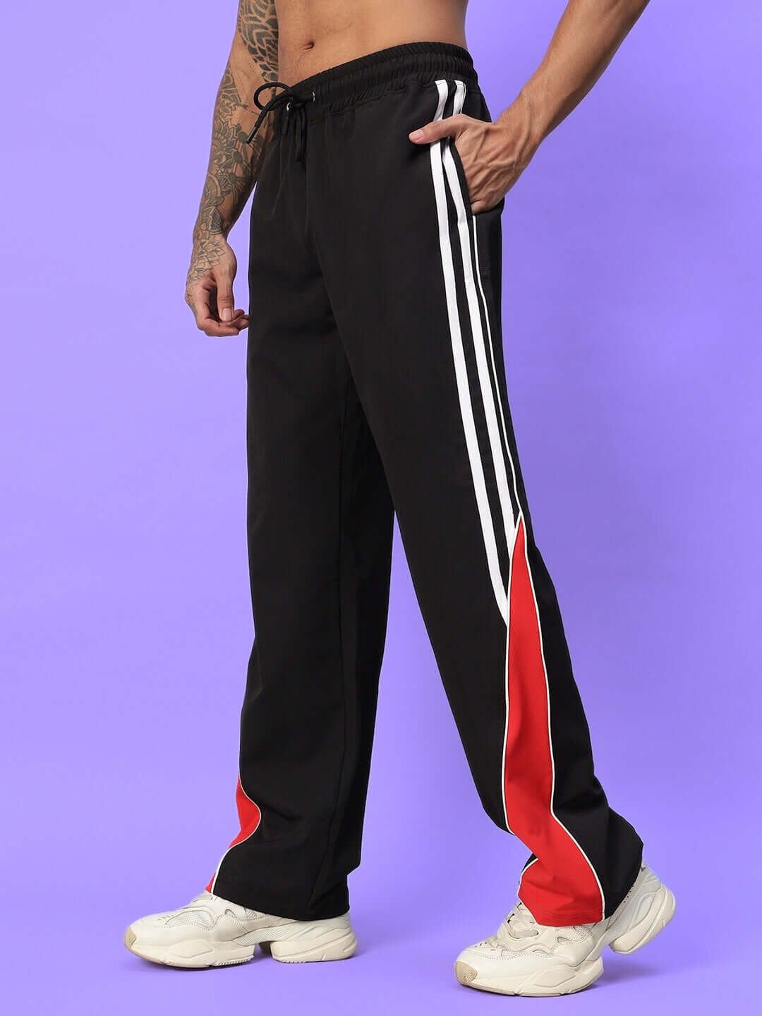 Man wearing black parachute cargo pants with white and red stripe detail on purple background