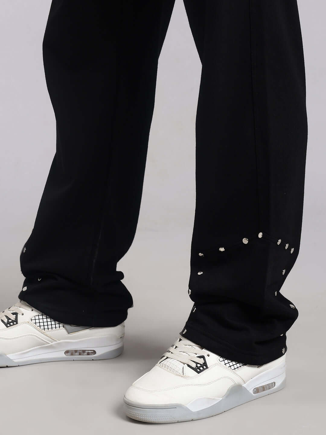 Model wearing black relaxed fit jogger by DUDS, showcasing studded detail above white sneakers.