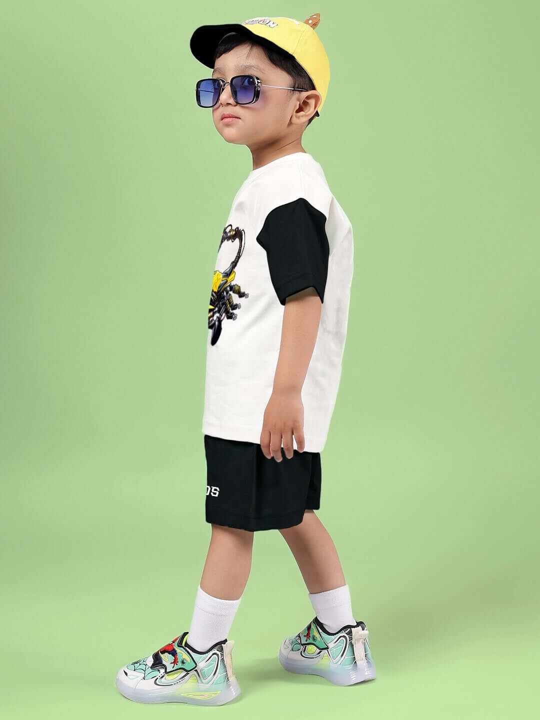 Child wearing STYLISH ROBOT CO-ORD FOR BOYS & GIRLS OFF WHITE BLACK set with sunglasses on a green background.