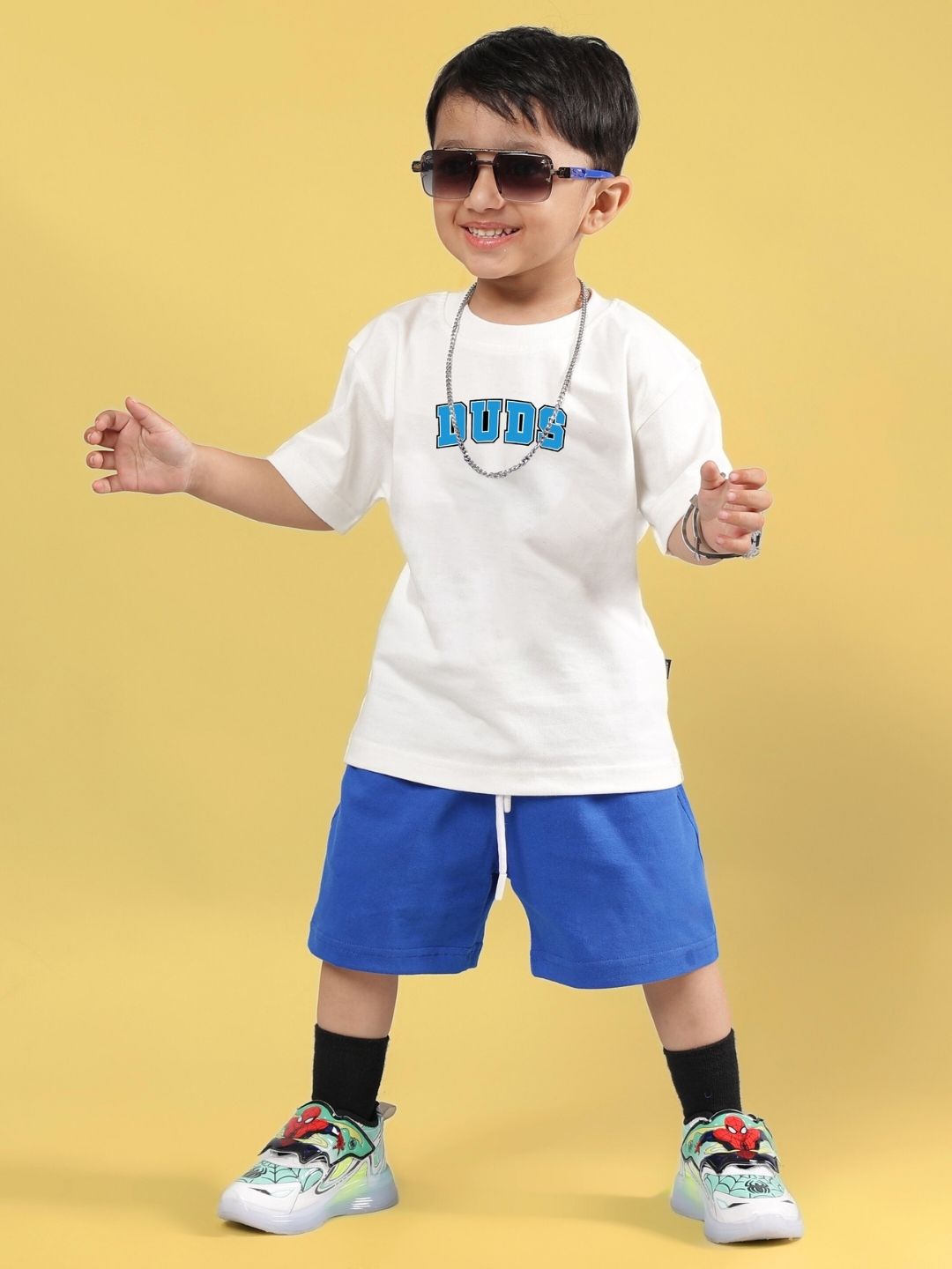 SUPER AWESOME T-SHIRT FOR BOYS AND GIRLS OFF WHITE shown on a child wearing blue shorts and sneakers, posing against a yellow background.