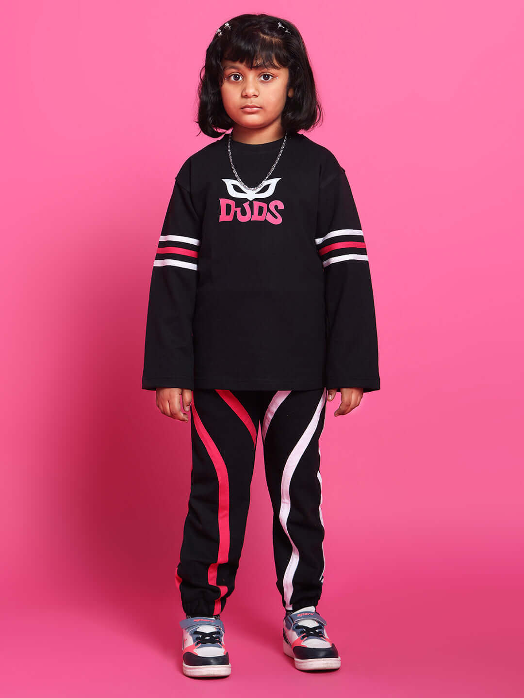 Child wearing SUPER CHAMP black co-ord set, featuring a premium cotton French Terry top and elastane pants on a pink background.