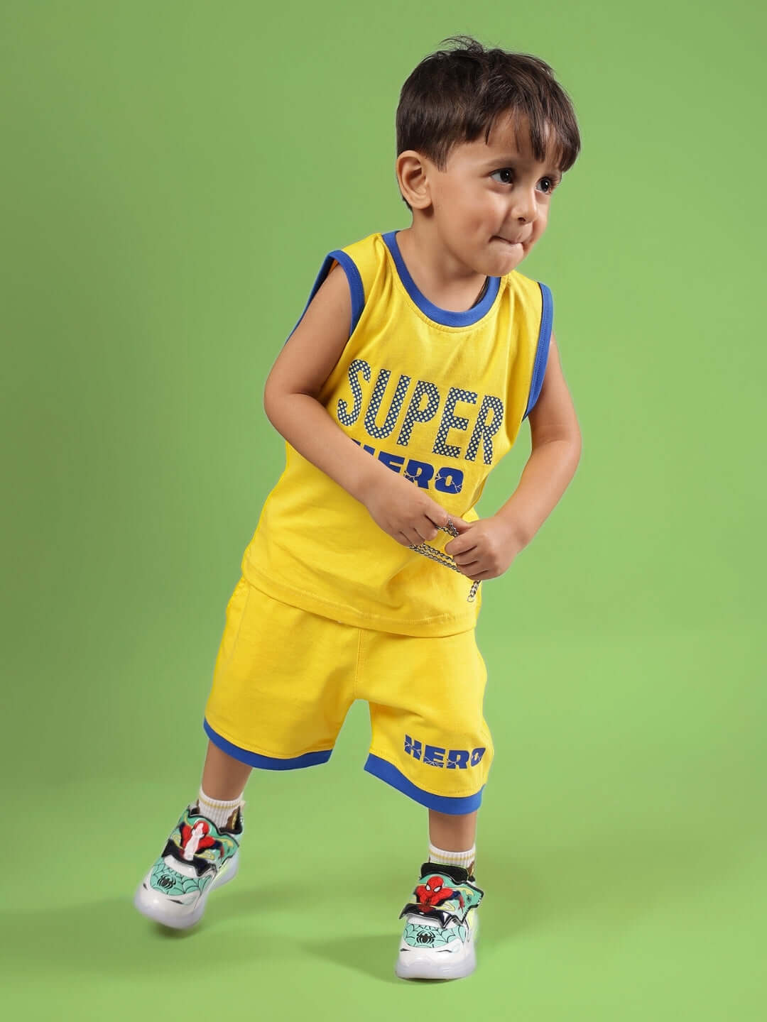 Alt Tag: Young boy wearing SUPER HERO CO-ORD FOR BOYS & GIRLS YELLOW outfit, featuring a vibrant yellow top and shorts, against a green background.