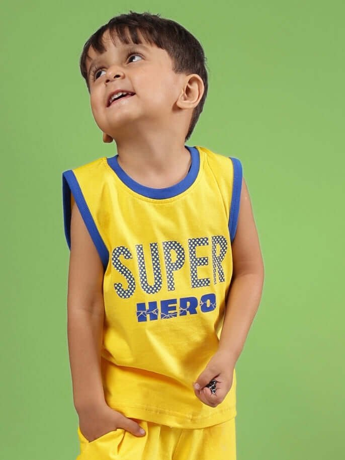 Young boy wearing a yellow Super Hero T-shirt for kids, with blue trim, smiling against a green background.
