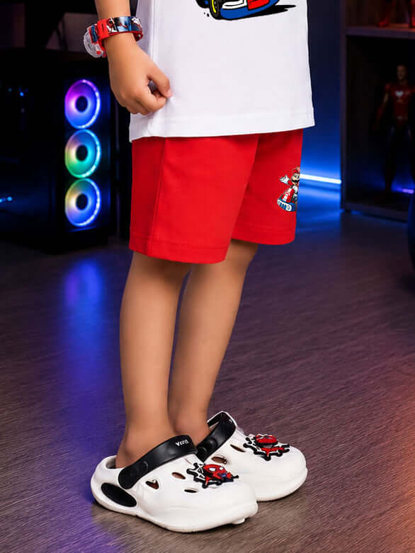 A child wearing SUPER MARIO COOL SHORTS FOR BOYS GIRLS RED, red shorts with a fun design, paired with white crocs.