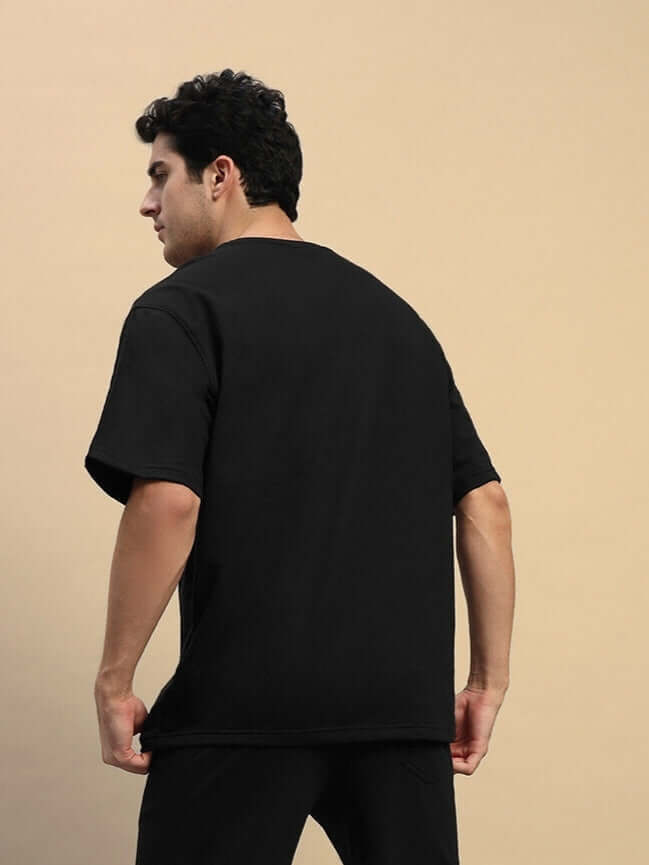 Back view of a black oversized T-shirt, crafted from premium heavy gauge fabric, worn by a person standing against a neutral background.