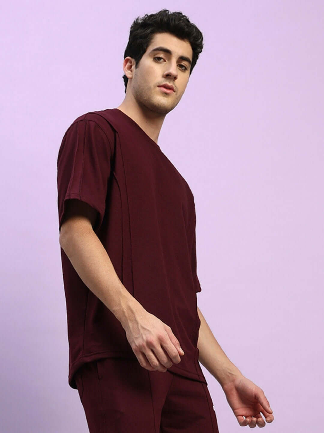 Model wearing Superior Oversized Maroon T-Shirt made of premium heavy gauge cotton fabric, shown from side view against a light purple background.