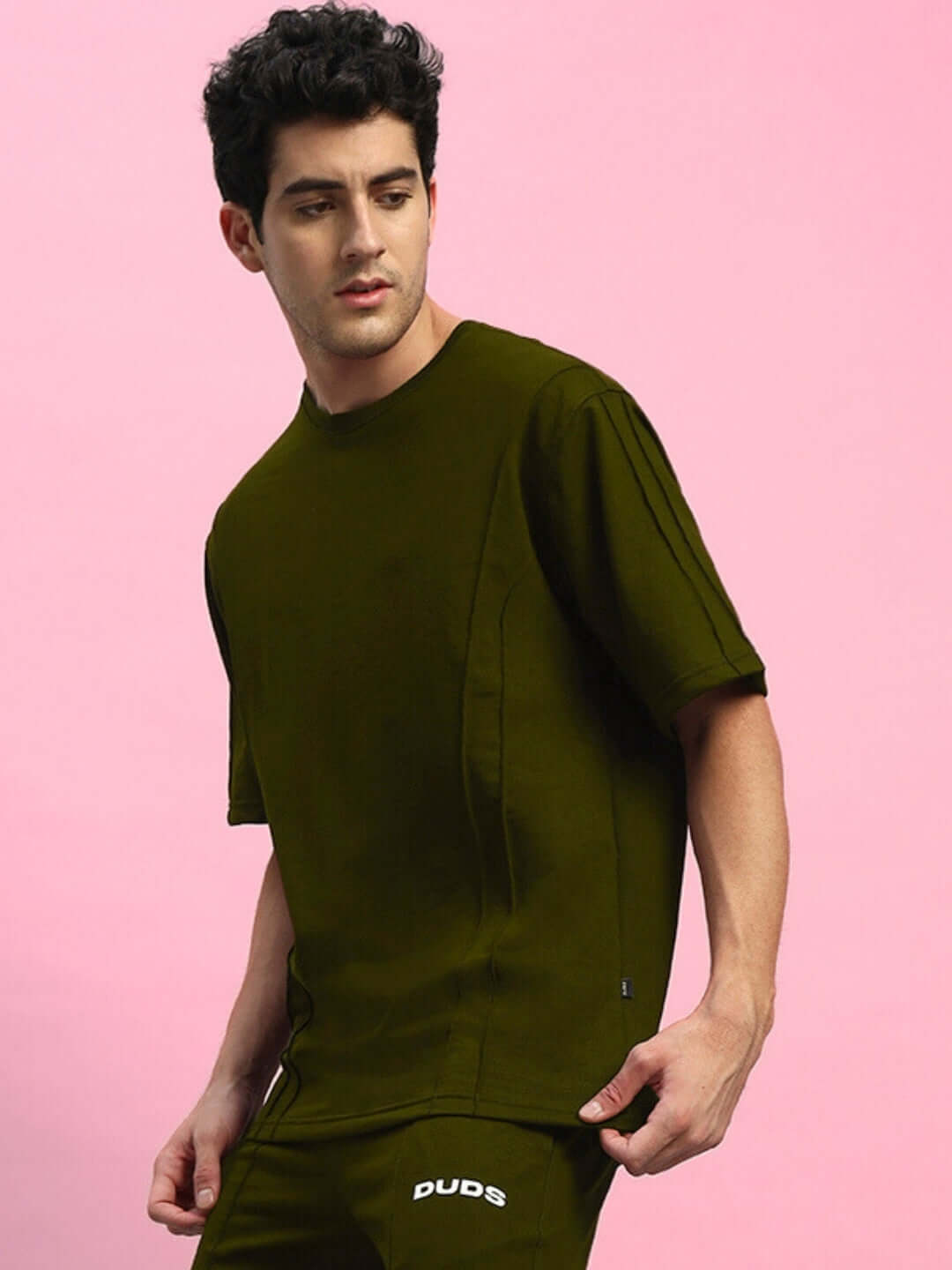 Model wearing an olive green oversized t-shirt made from 97% premium cotton and 3% elastane, against a pink background.