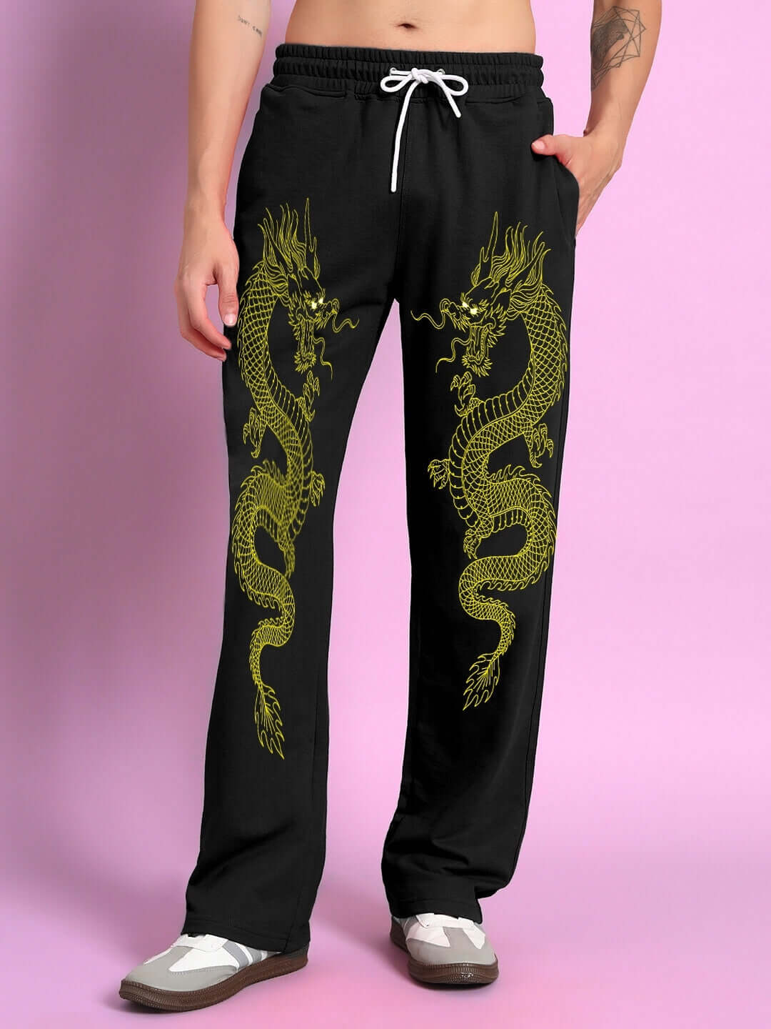 Man wearing black relaxed fit joggers with gold dragon print, pink background.
