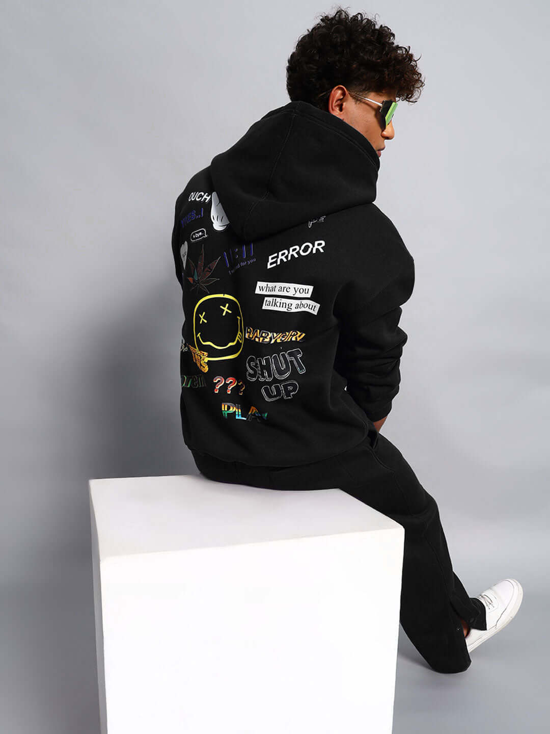 WEARDUDS SUPREME FLEECE HOODIE BLACK with colorful graphics and text, model sitting on white cube, custom fit available.