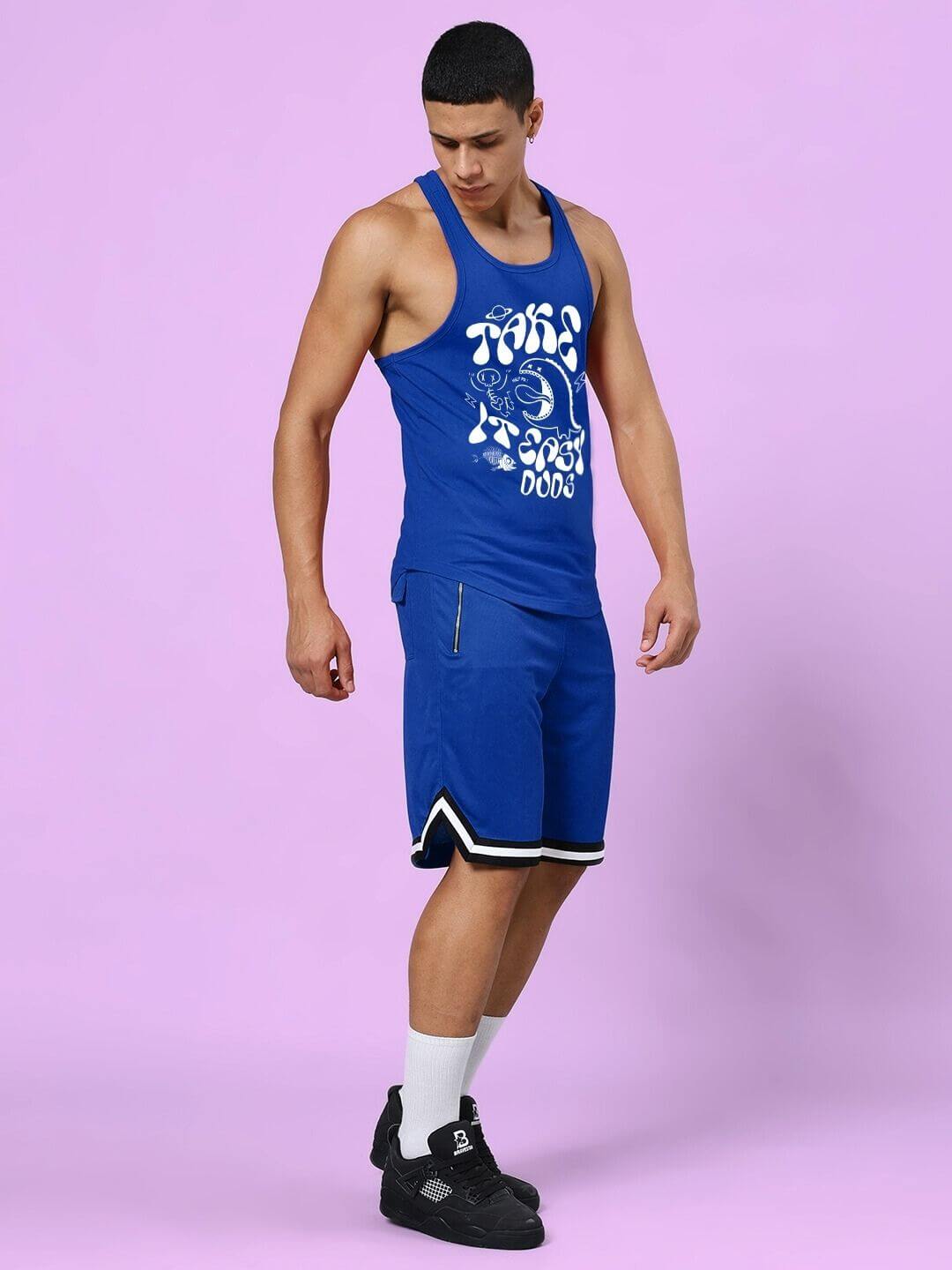 Man wearing a blue tank top and shorts on a purple background, showcasing the TAKE IT EASY GYM CO-ORD SET BLUE in a stylish pose.