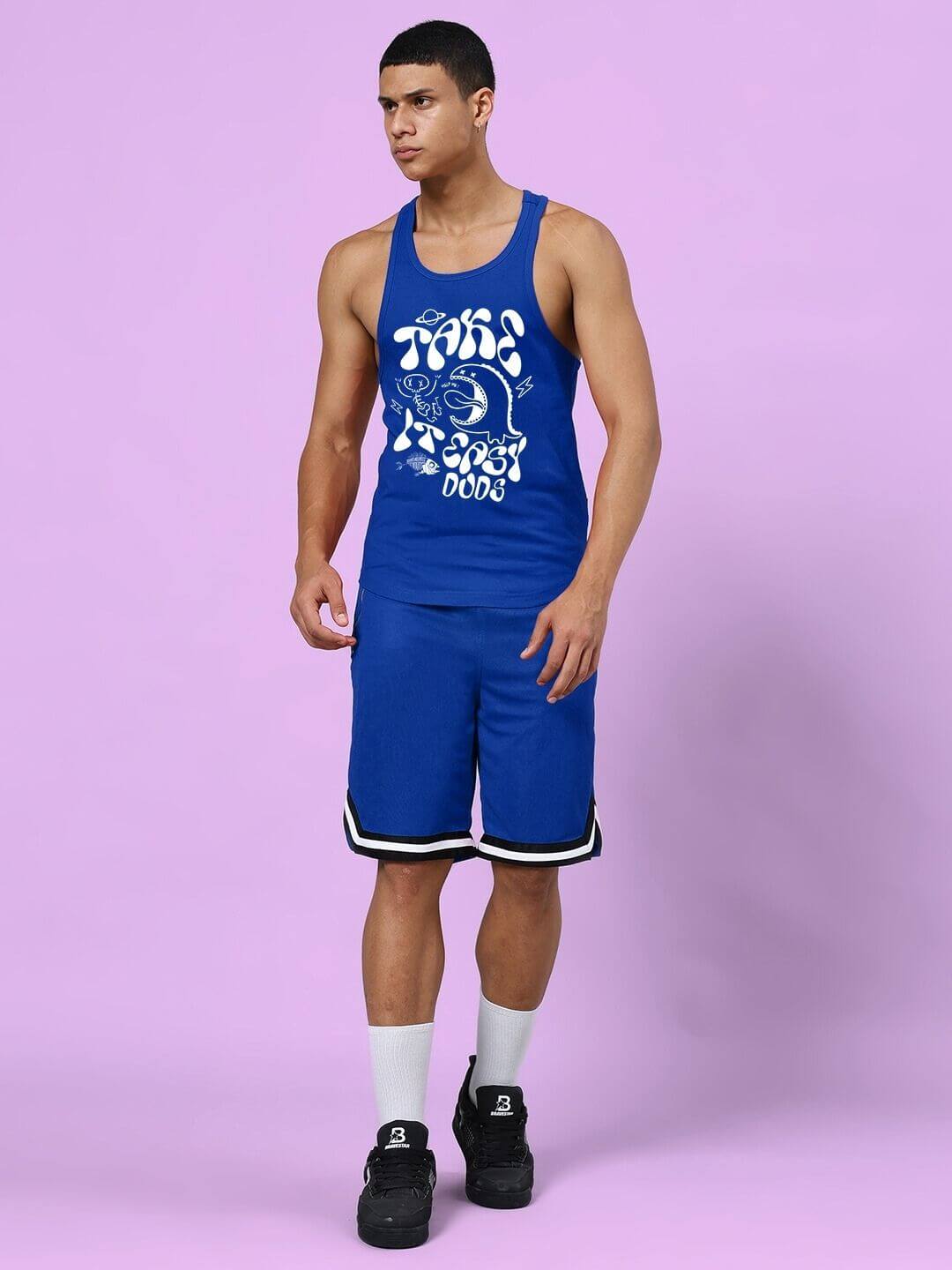 Man wearing TAKE IT EASY GYM VEST T-SHIRT BLUE, demonstrating sporty and casual style against a lavender background.