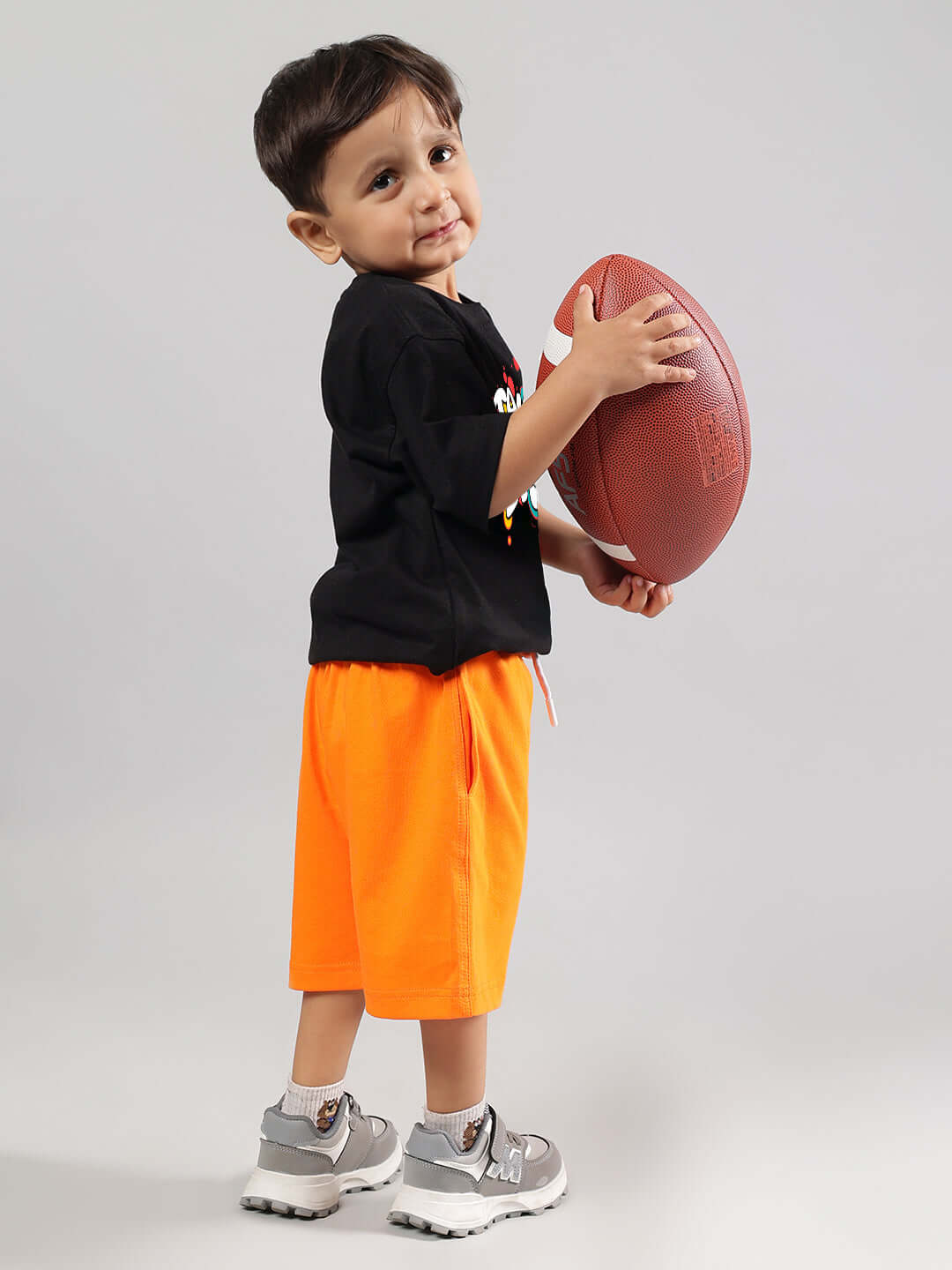 Child wearing TAKE THE STEP CO-ORD FOR BOYS GIRLS BLACK-ORANGE, holding a football