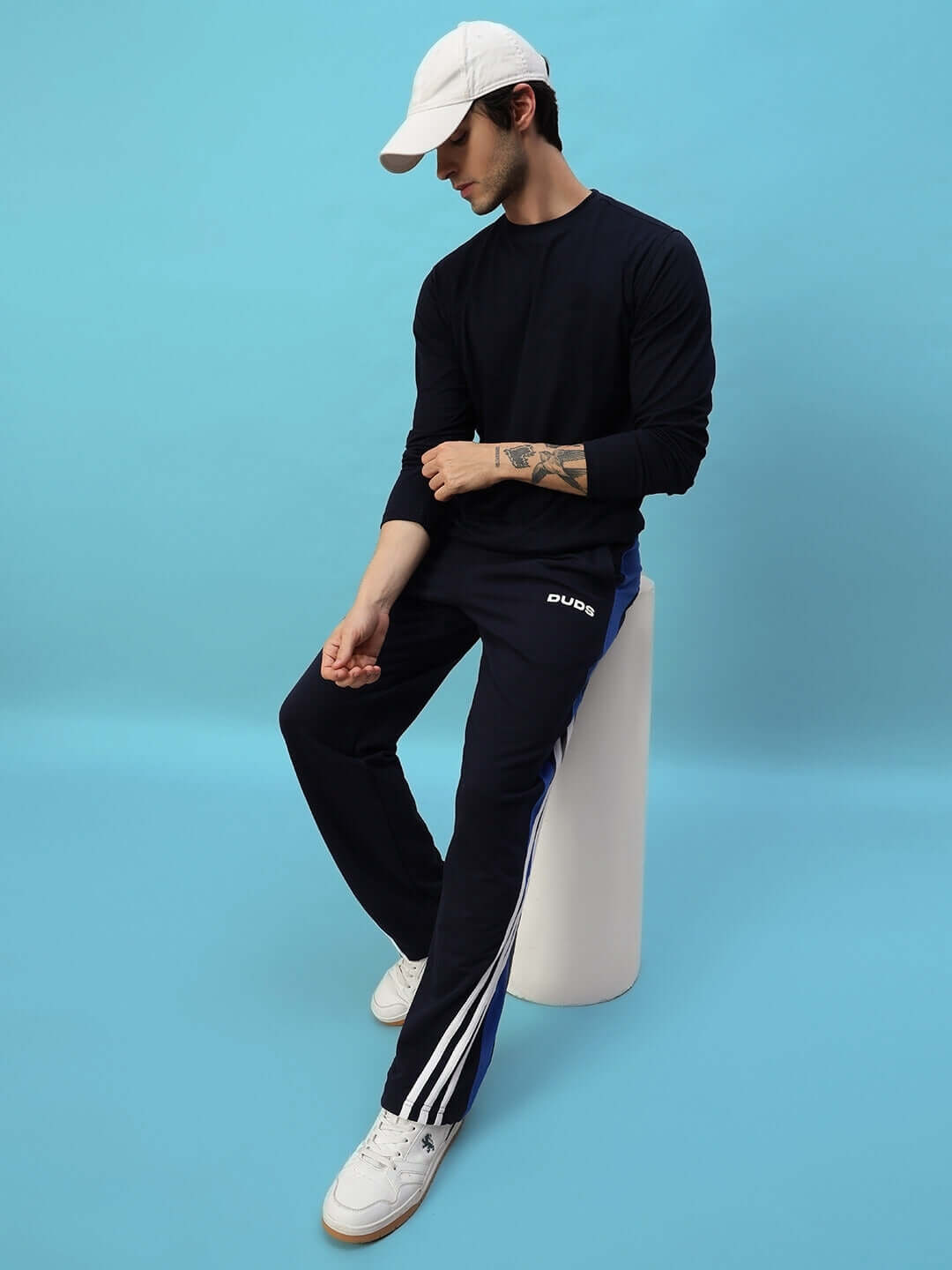 Model wearing TANGLE Relaxed-Fit Joggers in navy blue by DUDS, seated with casual style against blue background.