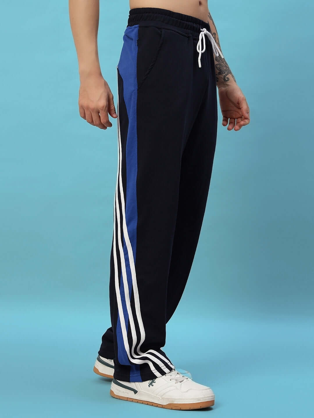 Navy blue Tangle relaxed-fit joggers with white and blue stripes, modeled against a blue background.