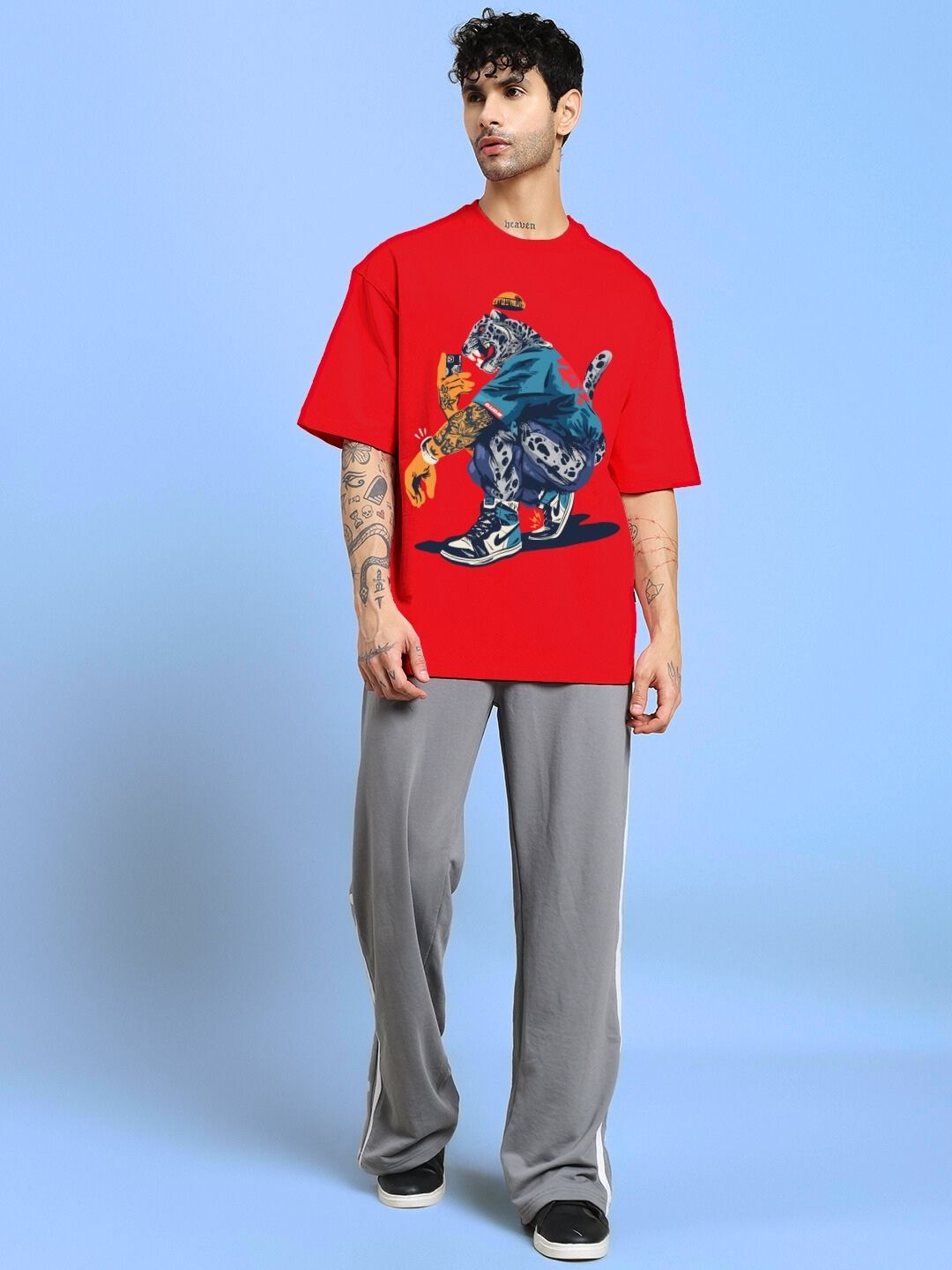 Model wearing TEKKEN KING T3 OVER-SIZED T-SHIRT RED with graphic featuring TEKKEN character, standing against a blue background.