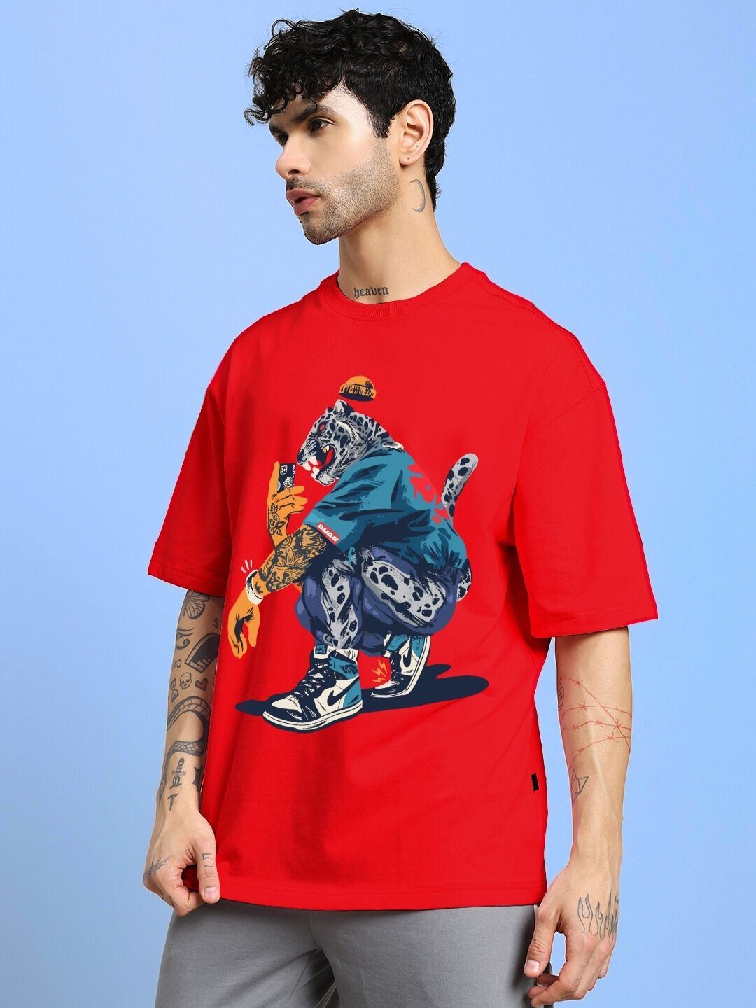Person wearing TEKKEN KING T3 OVER-SIZED T-SHIRT RED with graphic design, standing against a blue background.