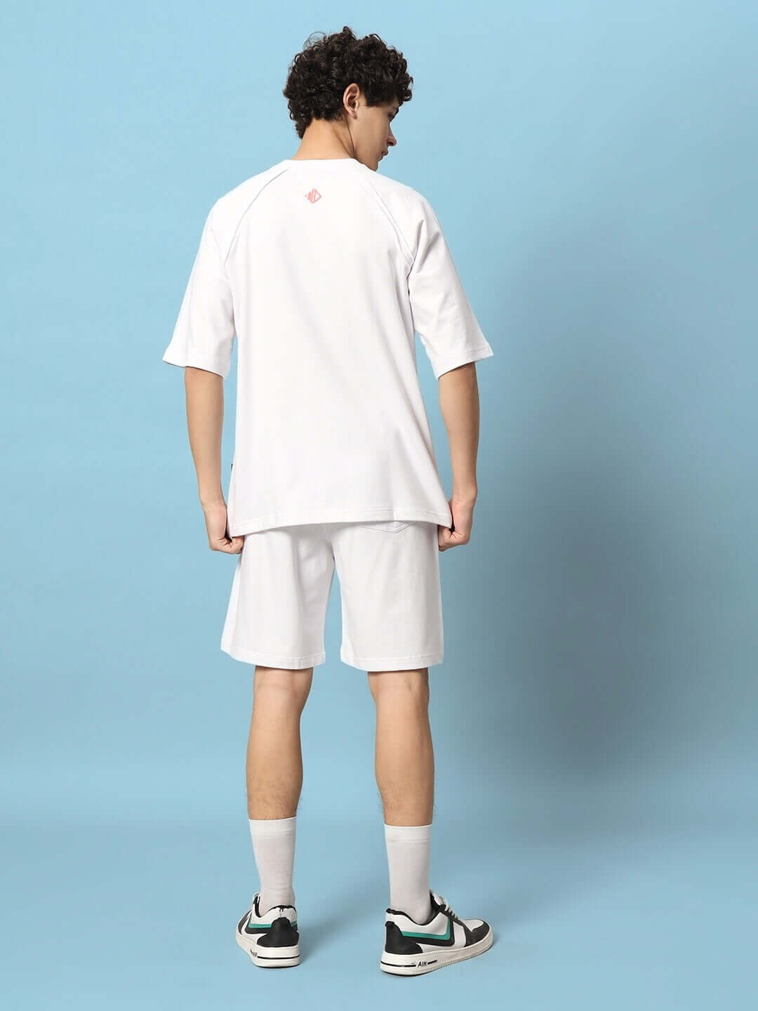 Model wearing a white co-ord set titled "The World Is Mine," featuring a premium cotton blend, viewed from the back against a blue background.
