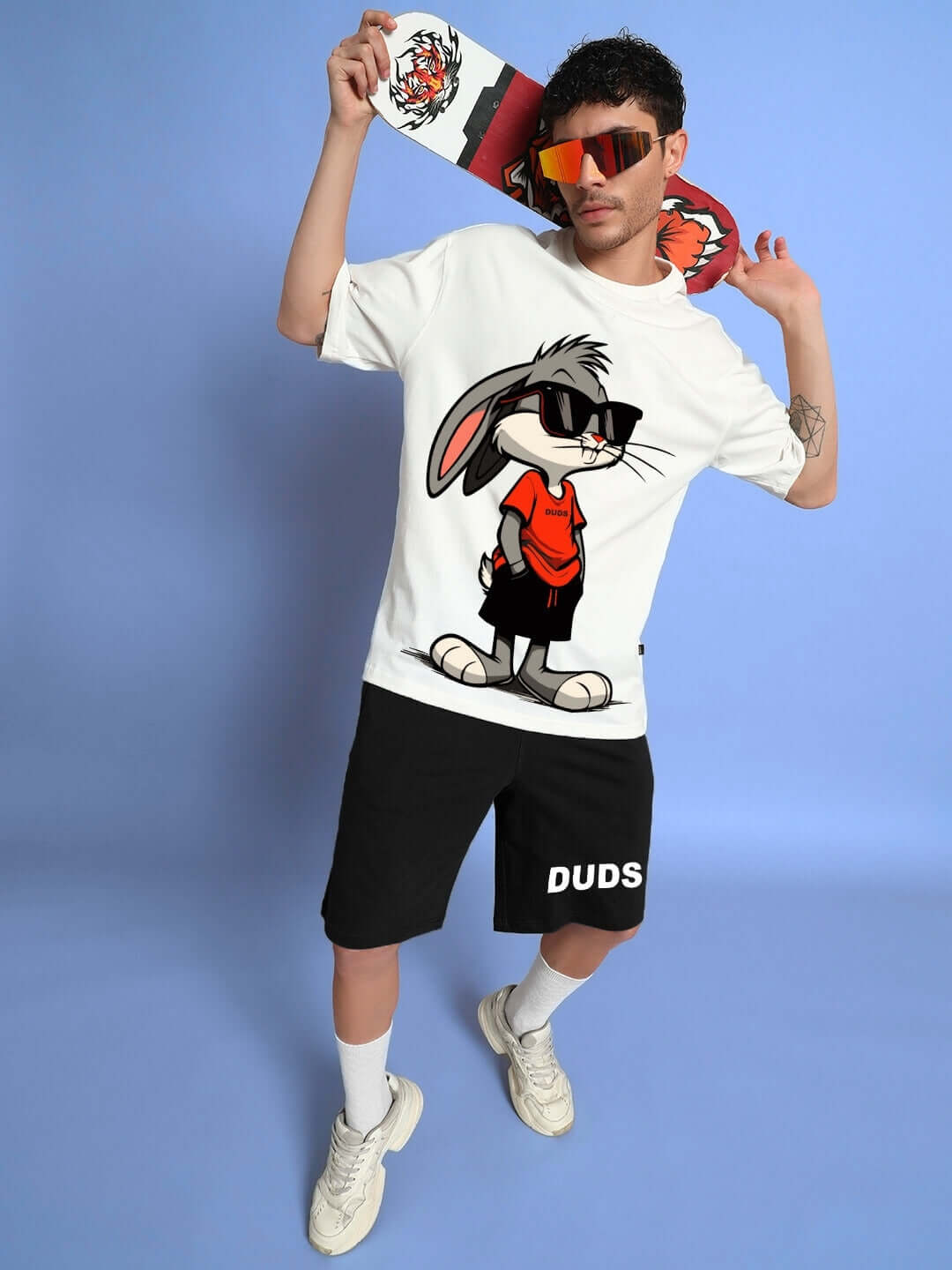 Man wearing off white black THINK BIG BUNNY TOONS CO-ORD SET with cartoon print, holding graphics, posed against a blue backdrop.
