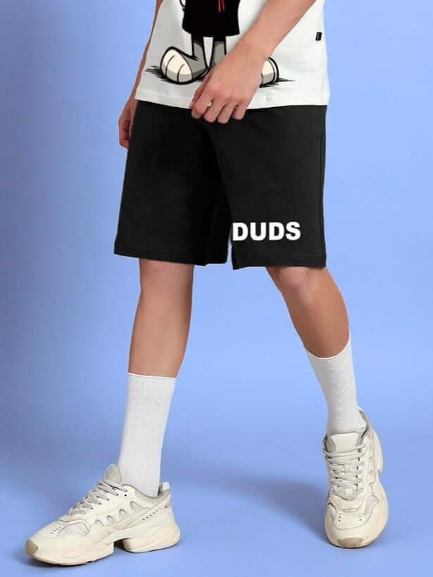 Model wearing THINK BIG SUMMER COTTON SHORTS BLACK with casual sneakers against a blue background.