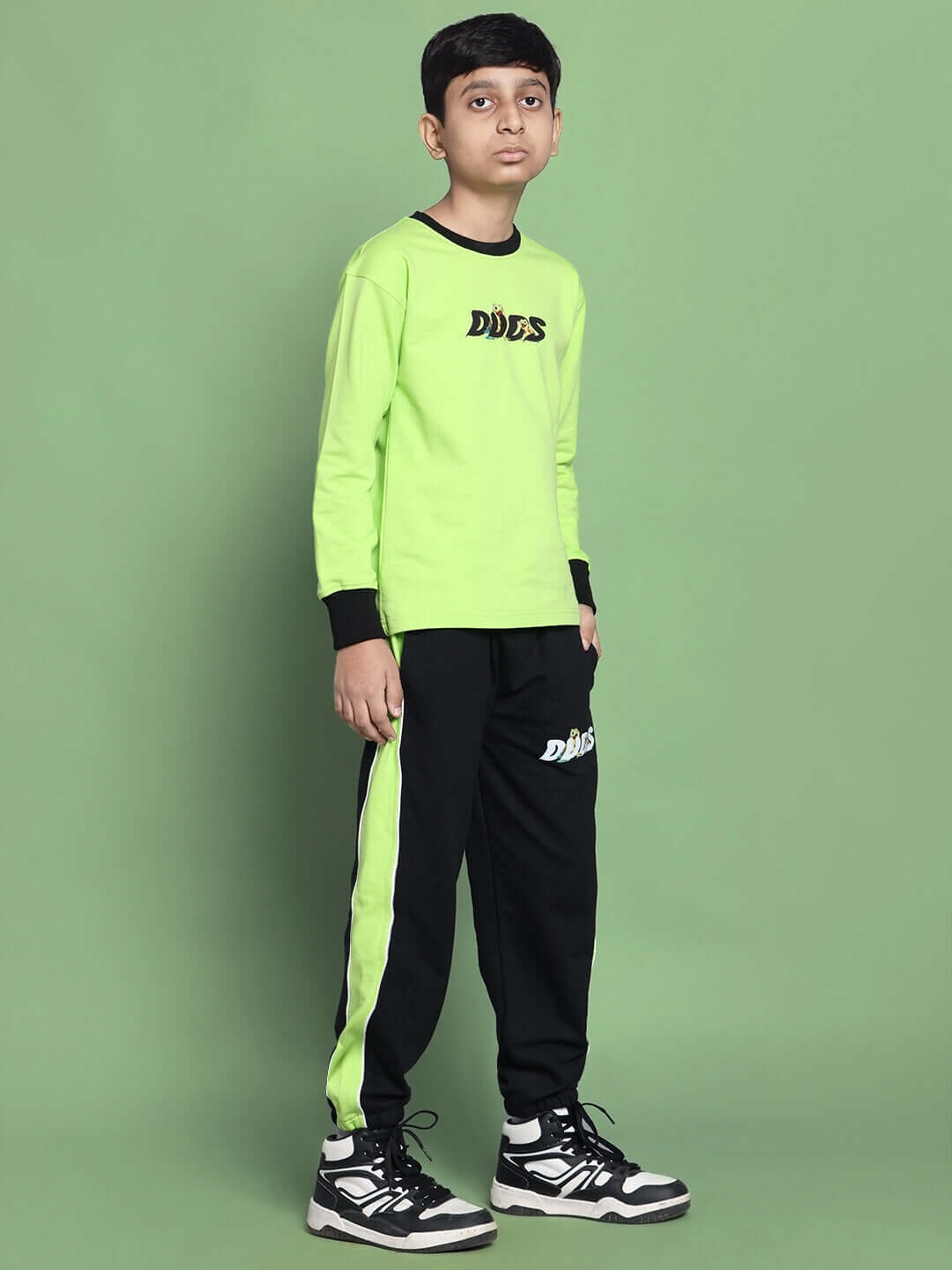 Boy wearing TILLY OVERSIZED CO-ORD SET FOR BOYS GIRLS NEON GREEN with black trim and pants, posing against a green background.